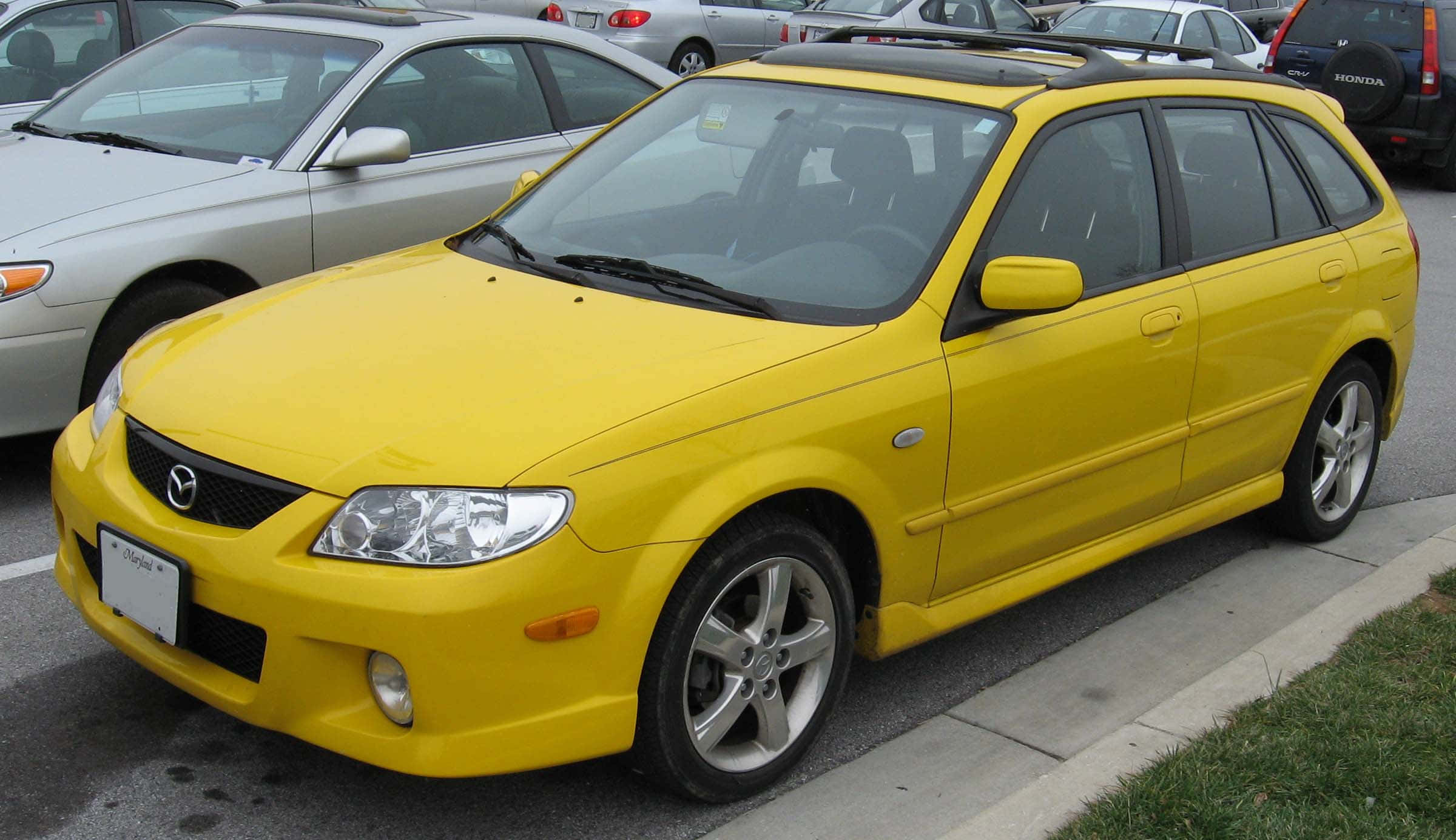 Mazda Protege 桌布 壁紙 — 一輛亮黃色的Mazda 3旅行車停在停車場，背景可見其他車輛。