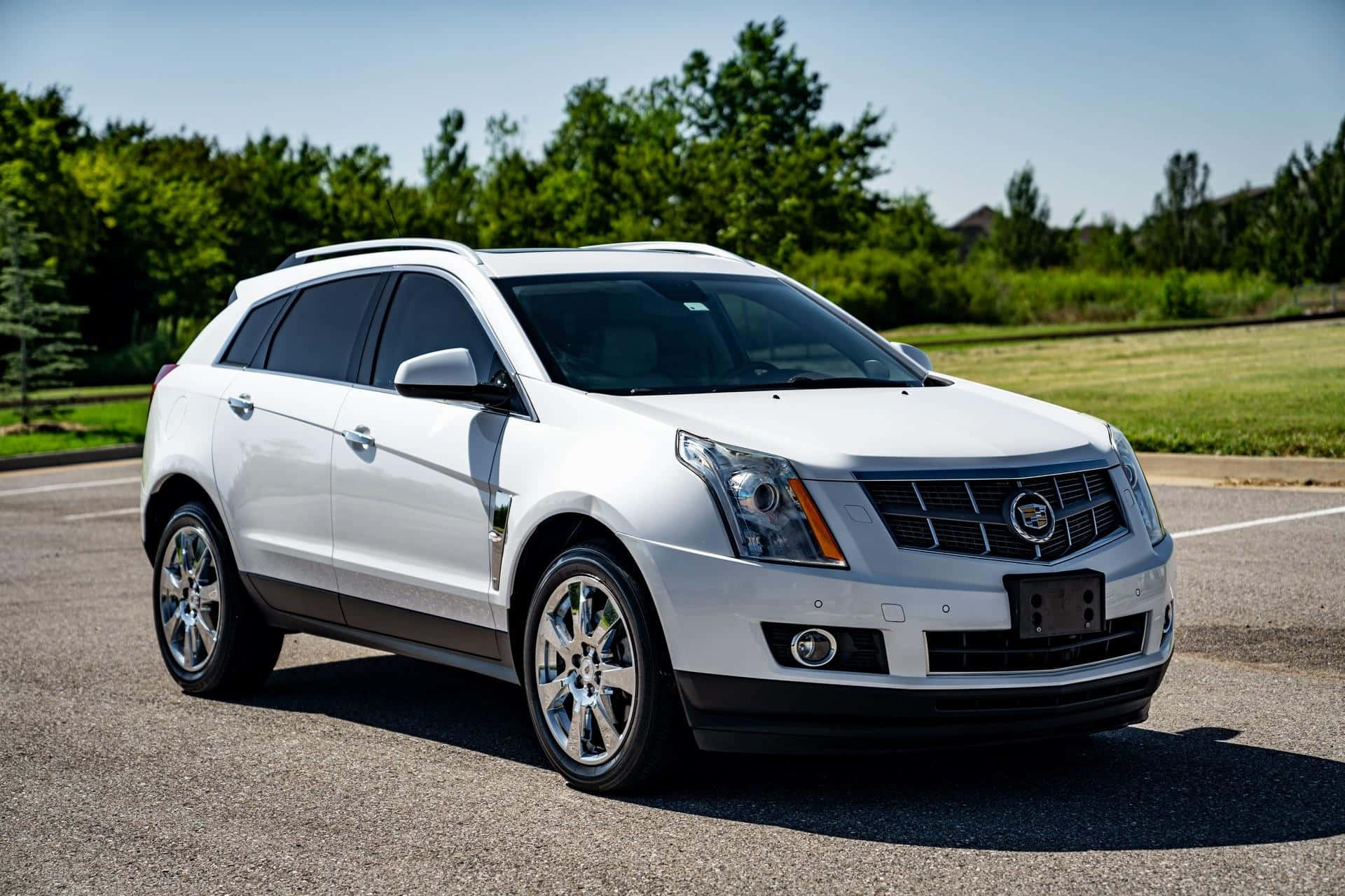Cadillac Srx 桌布 壁紙 — 一輛純白色的 Cadillac SRX SUV 停泊在瀝青路上，周圍有茂密的綠樹和草地，天空湛藍清澈。