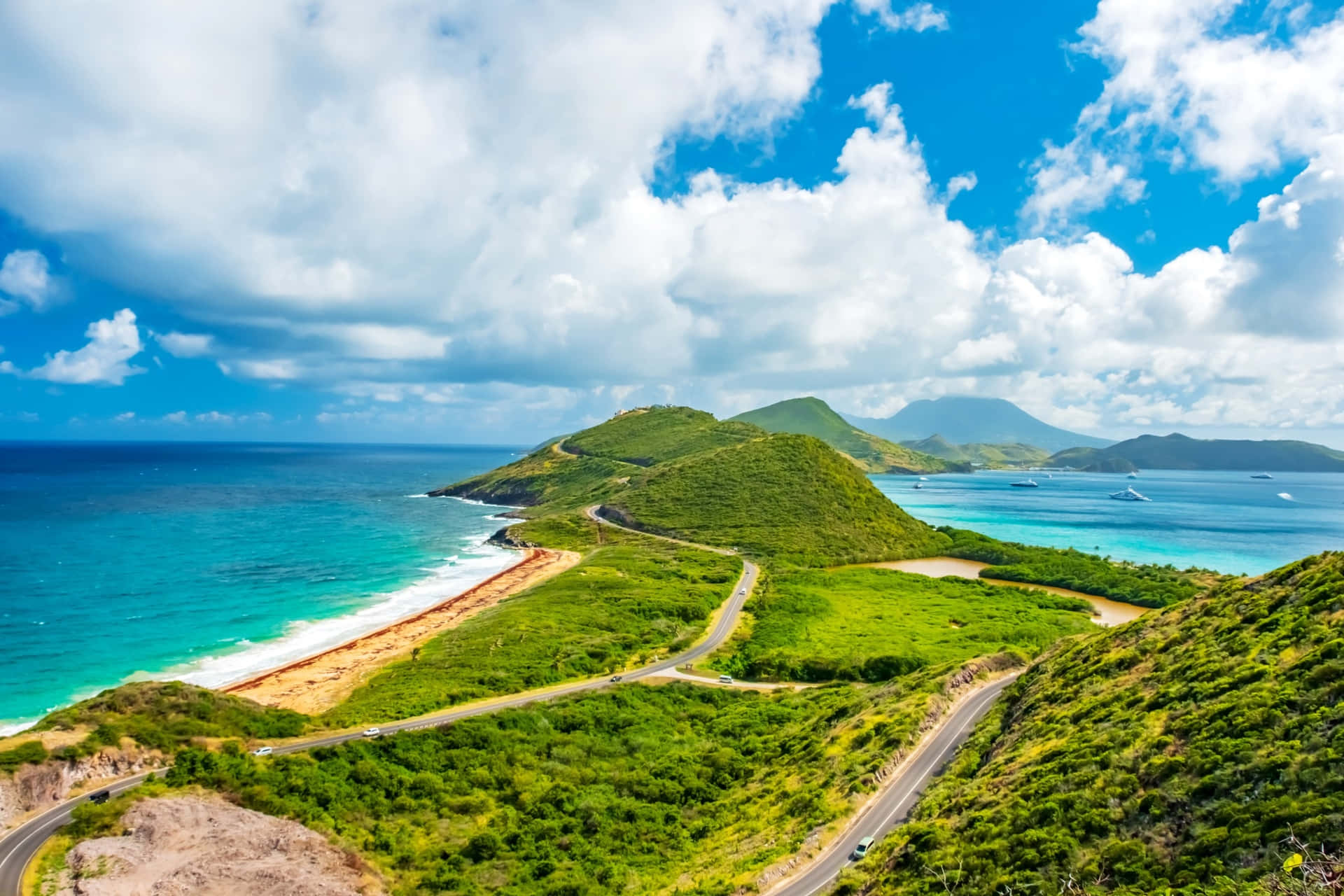  壁紙 — 一條蜿蜒的海岸公路擁抱著翠綠的山丘，旁邊是碧綠的海水，上方是明亮的藍天和蓬鬆的白雲。