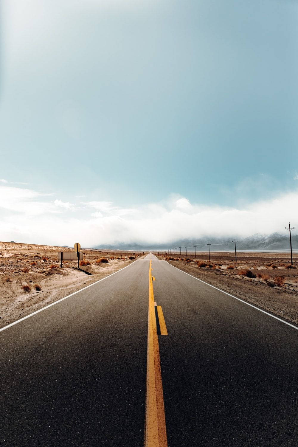 一條空蕩蕩的道路穿過沙漠景觀，遠處有山脈，在藍天下。