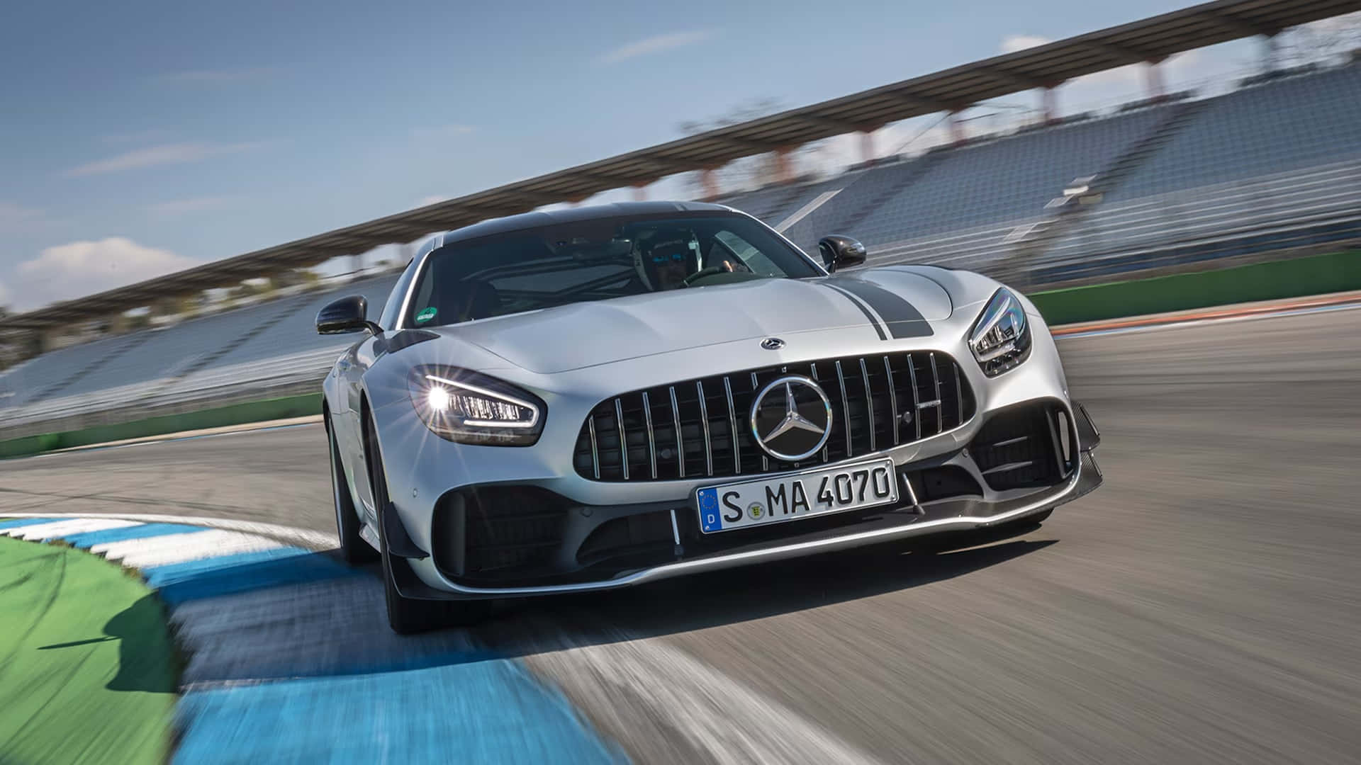  壁紙 — 一輛銀色 Mercedes-AMG GT R 在賽道彎位高速行駛，背景有模糊的看台座位。