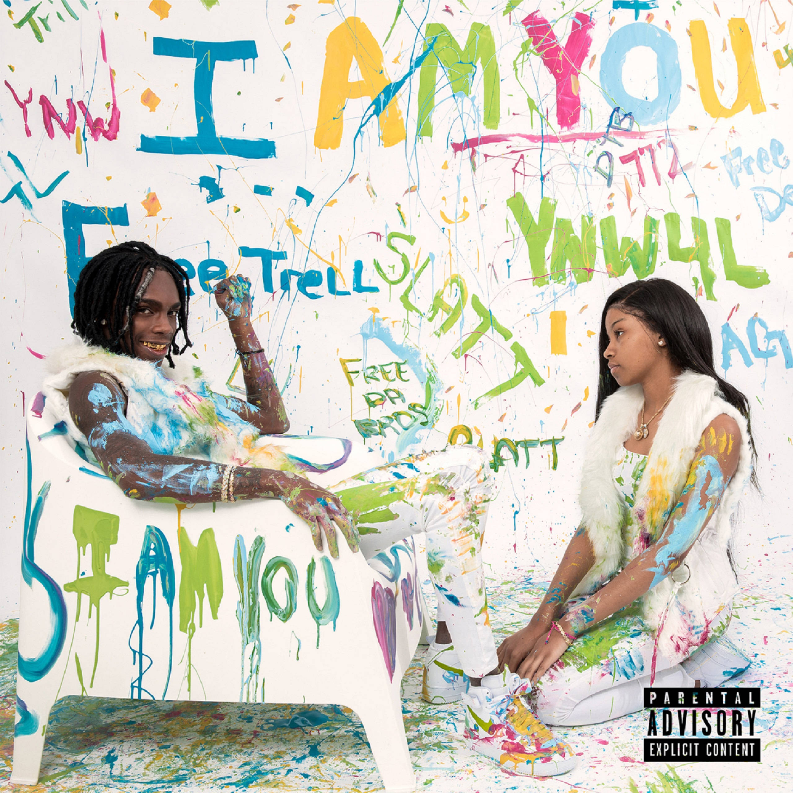 YNW Melly I Am You 混音帶 壁紙 — 兩位滿身油漆的藝術家背靠著佈滿塗鴉、帶有粗體彩色文字的牆壁相對而坐。