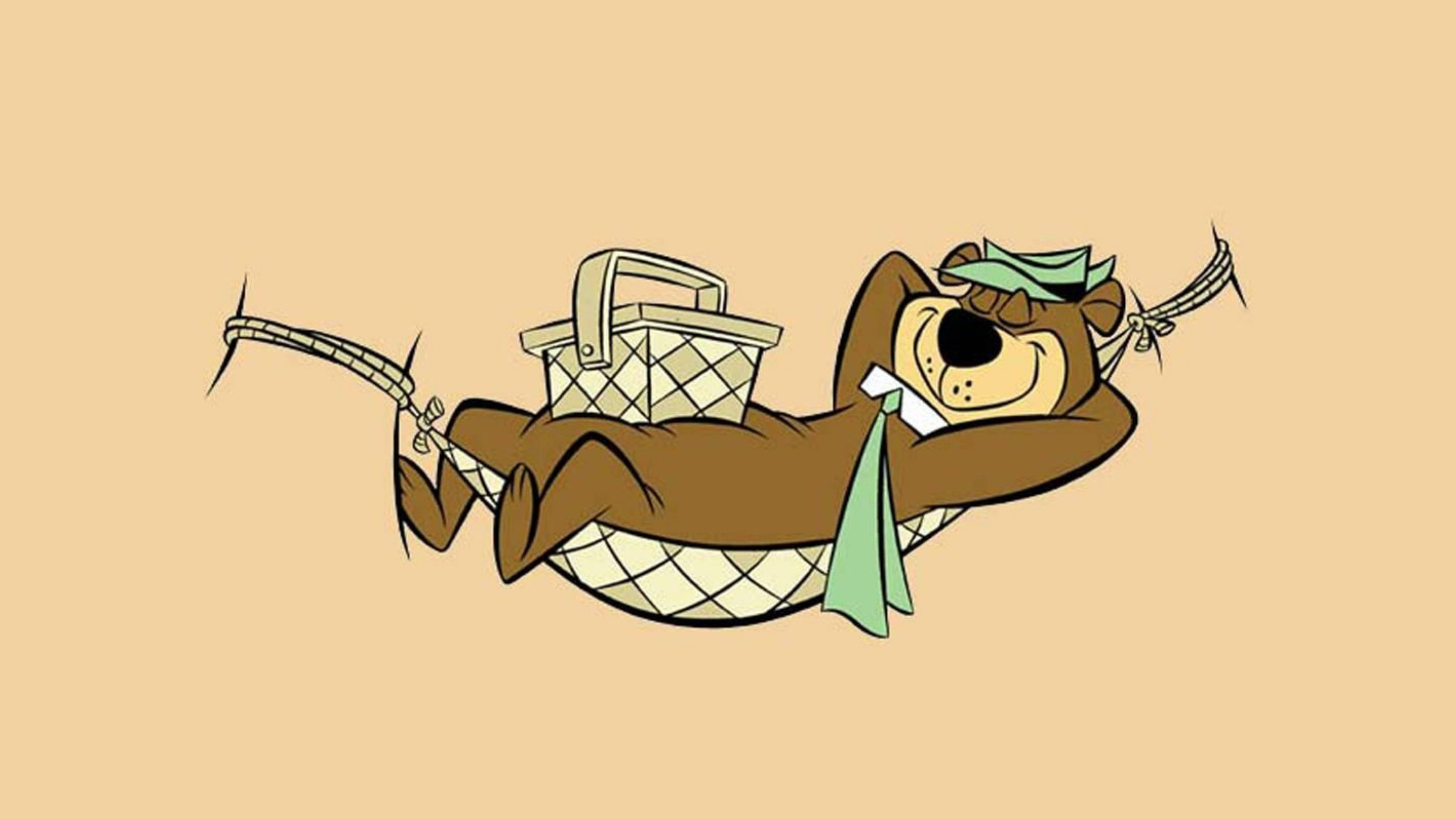 Yogi Bear 在吊床上 壁紙 — 一隻卡通熊喺吊床上攤唞，旁邊有個野餐籃同綠色圍巾，背景係純米色。