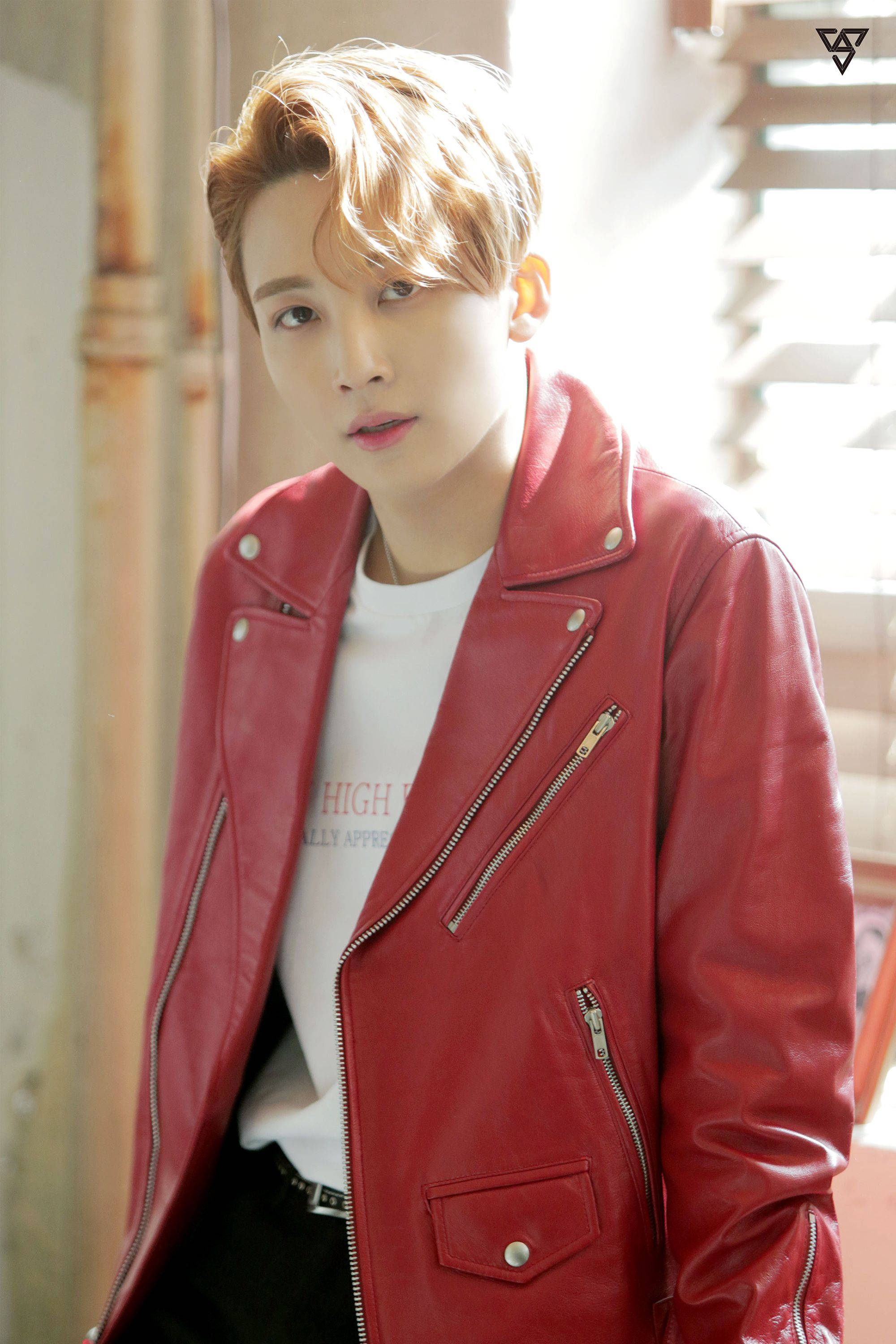 Yoon Jeonghan Call Call Call 壁紙 — 一位年輕男子，梳著時尚的金色頭髮，在陽光明媚的城市環境中，身穿白色T恤外搭一件亮面紅色皮夾克。