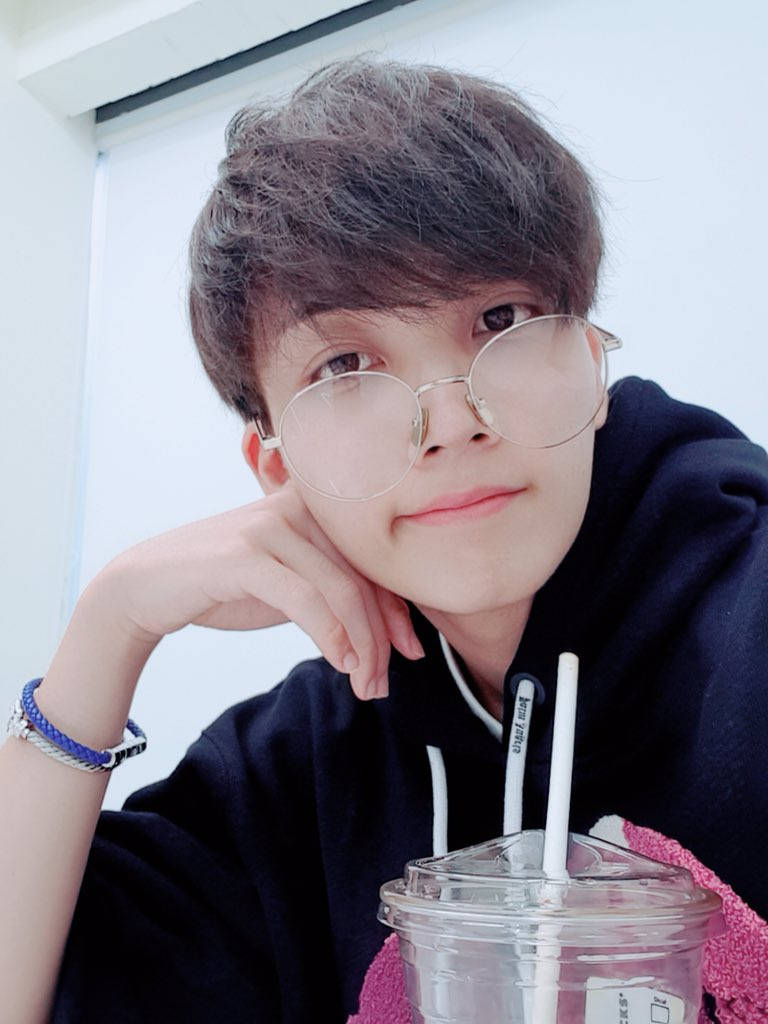 Yoon Jeonghan 戴眼鏡自拍 壁紙 — 一位戴眼鏡的年輕人，在明亮的室內環境中，將下巴擱在手邊，旁邊放著一杯飲料。