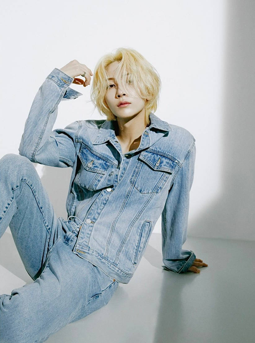 Yoon Jeonghan 牛仔配牛仔 壁紙 — 一位金髮人物穿著牛仔服裝，在純白背景和戲劇性燈光下隨意坐著。