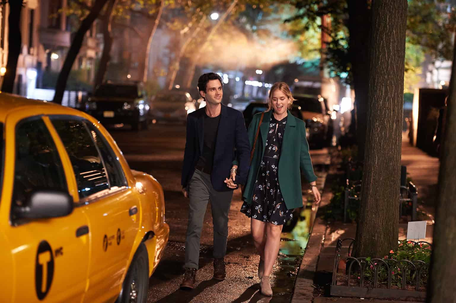 《You》中Joe與Love夜間散步場景 壁紙 — 一對情侶手拖手在夜晚濕漉漉的城市行人路上走過一輛黃色的士，街燈投射出溫暖的光芒。