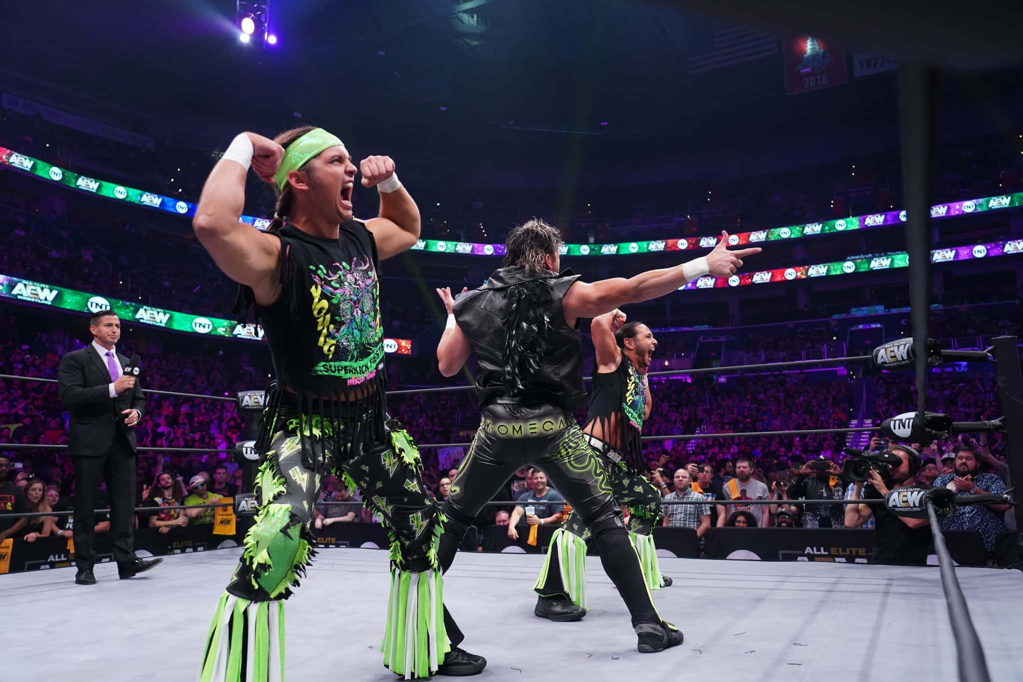 Young Bucks 馬特·傑克森與肯尼·歐米加 壁紙 — 兩名身穿螢光綠色和黑色裝備的摔角手在燈光明亮的擂台上慶祝勝利，周圍是歡呼的粉絲。