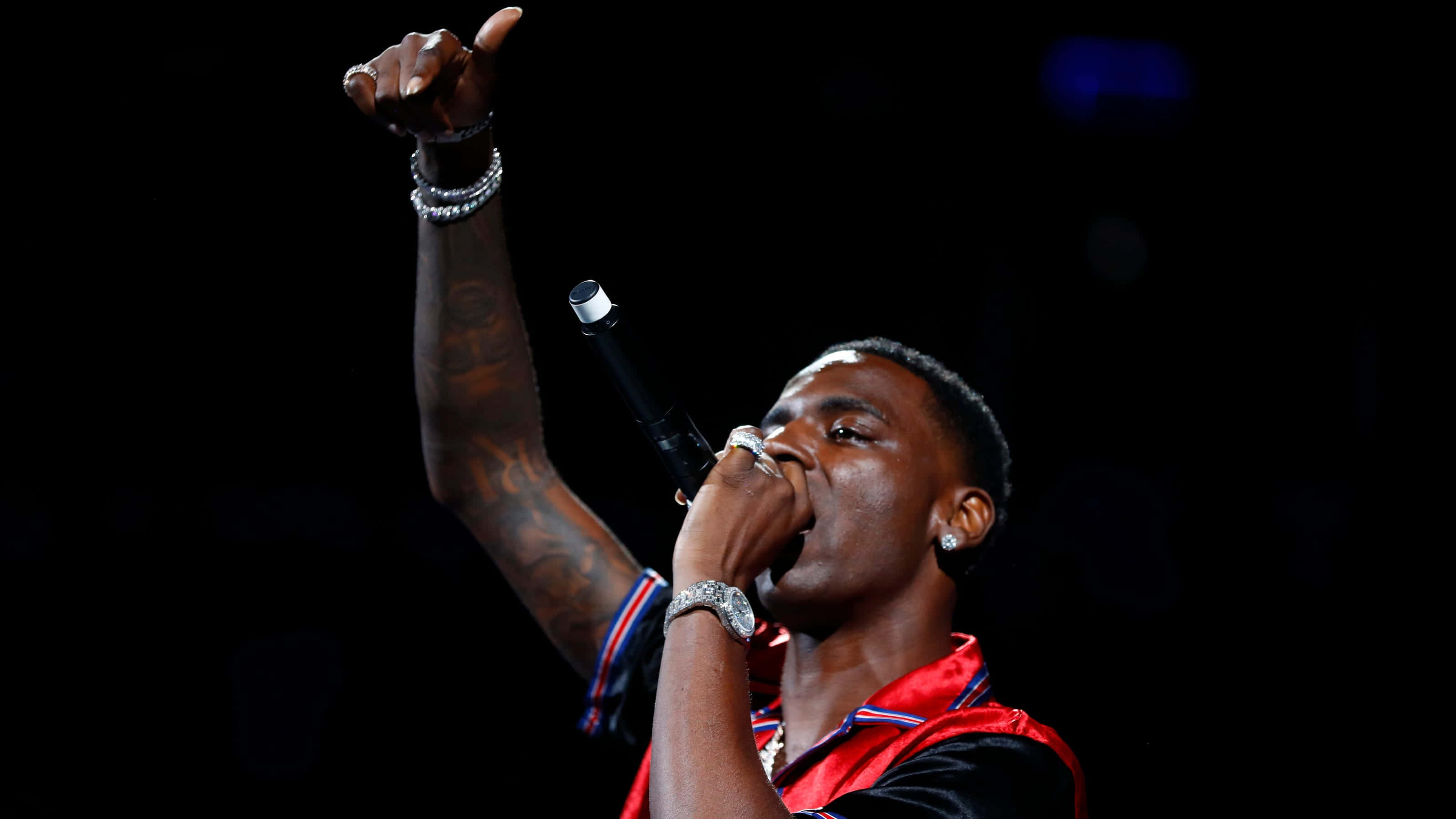 美國饒舌歌手 Young Dolph 2019 Memphis Madness 壁紙 — 一位男說唱歌手在明亮的舞台燈光下，以動態姿勢舉起一隻手臂，手持麥克風表演。