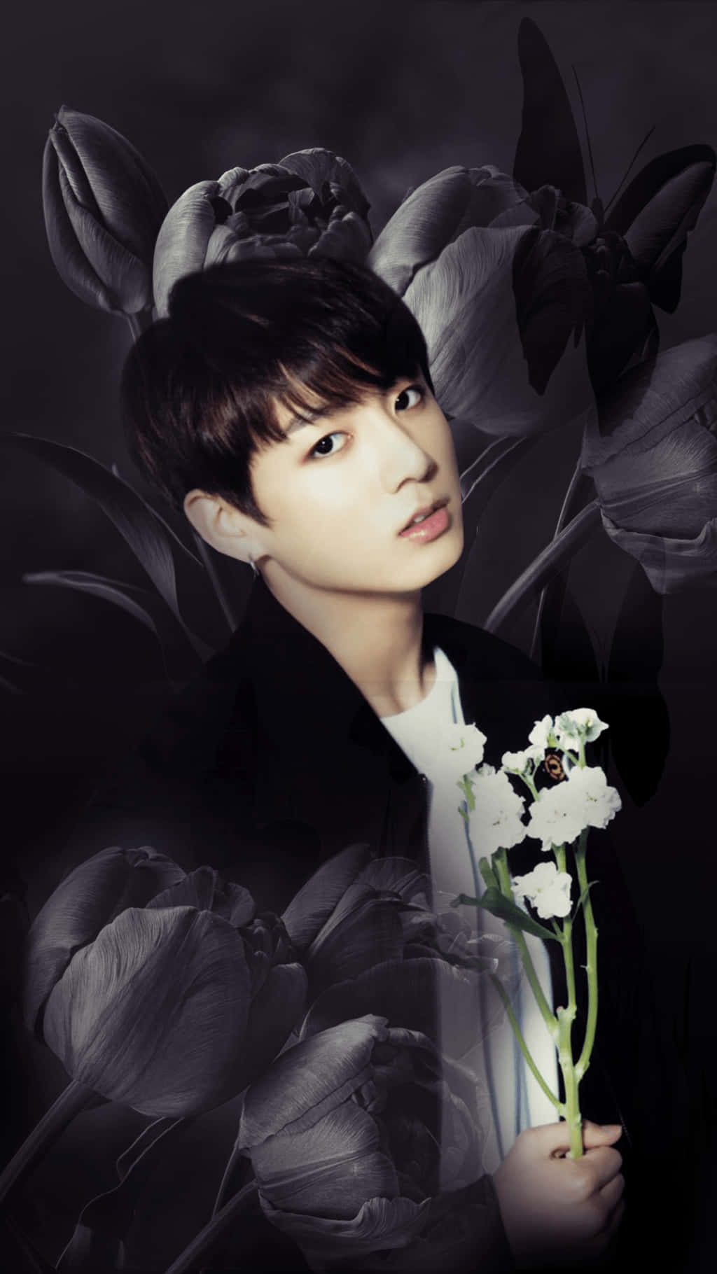 BTS Jungkook iPhone壁紙 壁紙 — 一個穿著黑色外套的年輕男子，在深色背景下手持白色花朵，背景中有大型灰色鬱金香和蝴蝶。