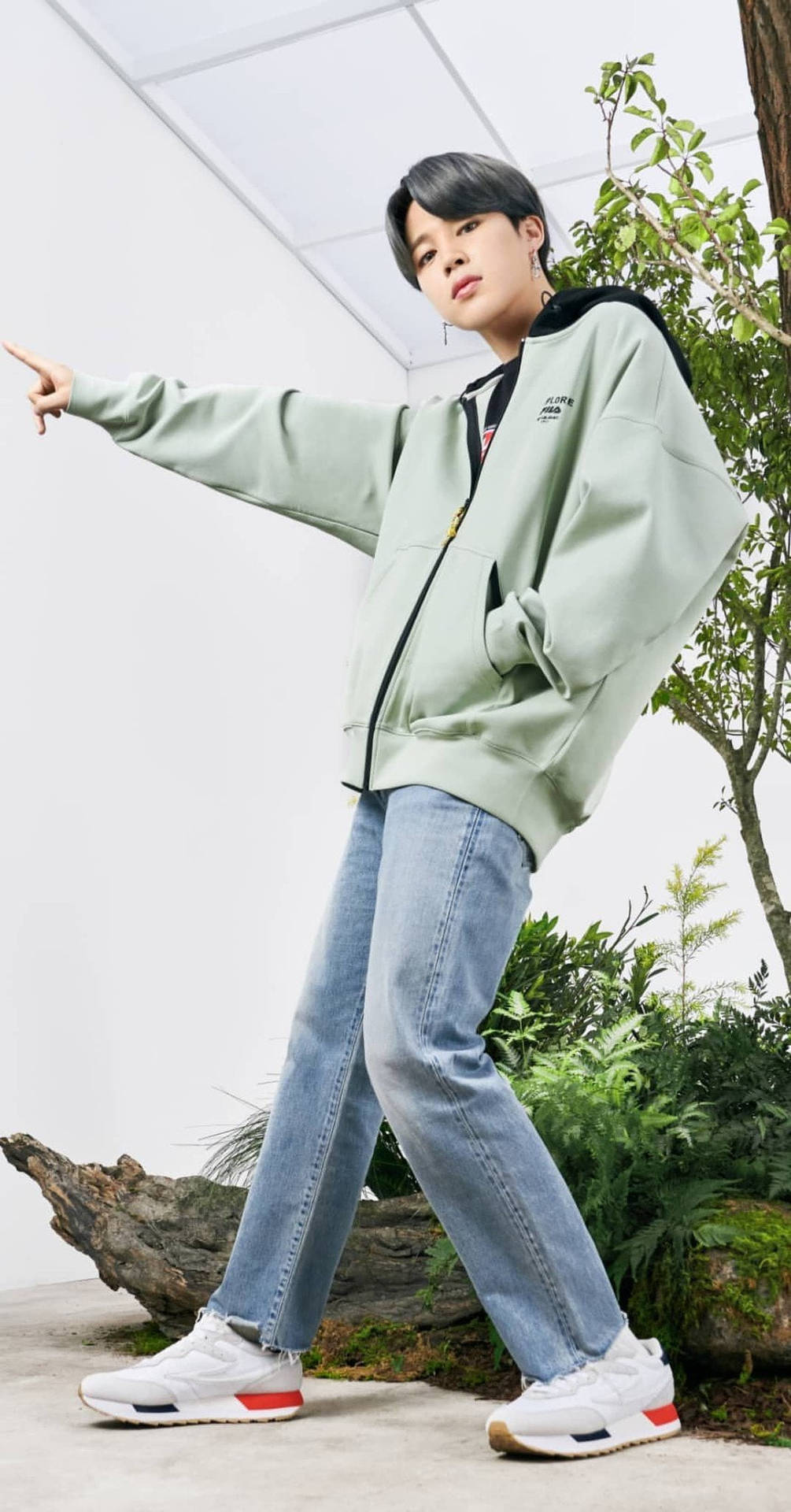 身穿綠色連帽衫和牛仔褲的年輕男子在植物附近戶外擺姿勢。