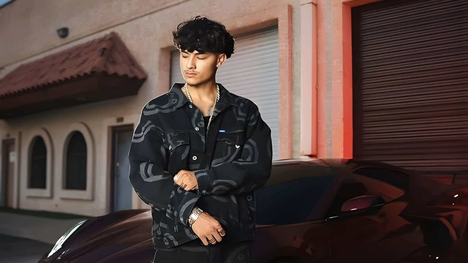  壁紙 — 一位身穿圖案外套的年輕男子自信地站在一輛時尚黑色跑車旁，背景是暖色調的城市建築外牆。