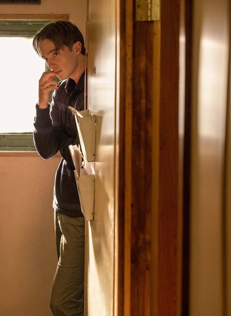  壁紙 — 一名年輕男子透過門口窺視，表情若有所思，背後窗戶透進溫暖的陽光。