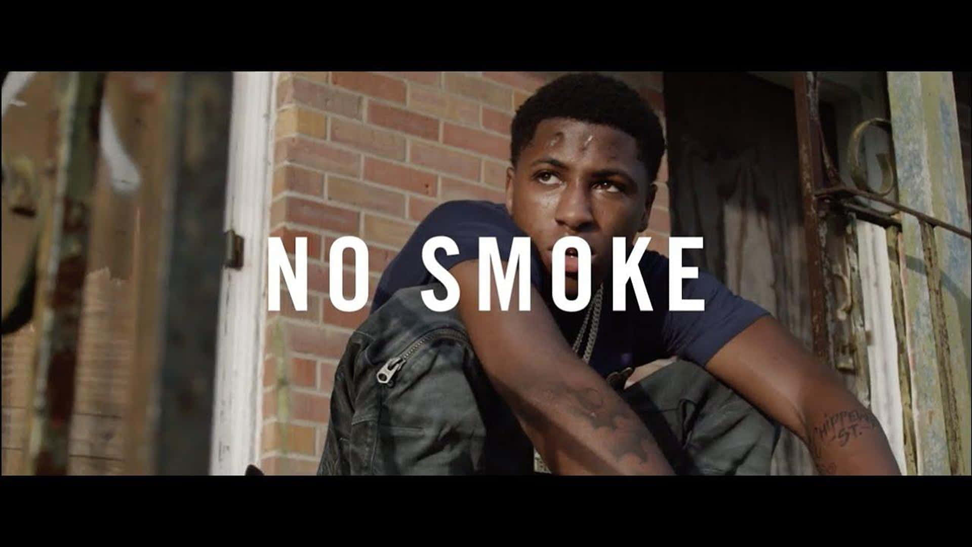 有紋身的年輕男子靠著有「NO SMOKE」文字的磚牆。