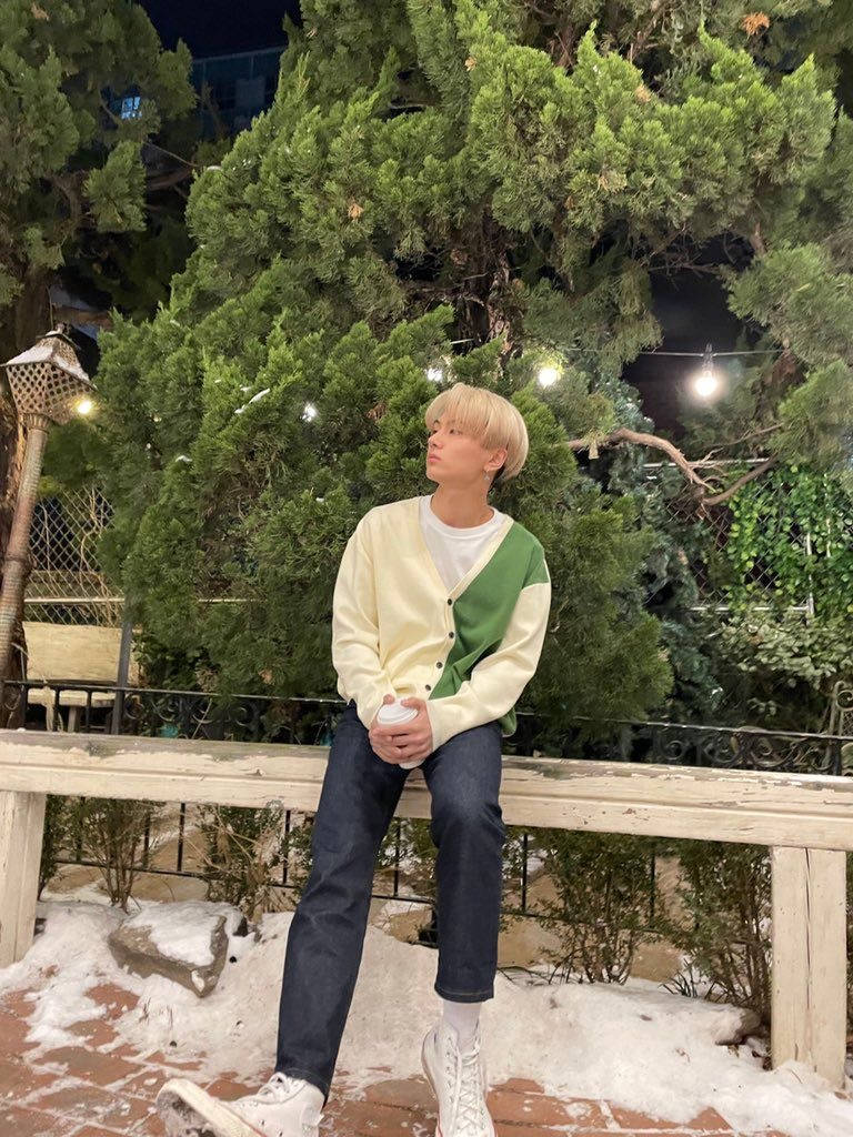 穿冬季外套的年輕人夜晚坐在有雪和綠樹的長椅上。
