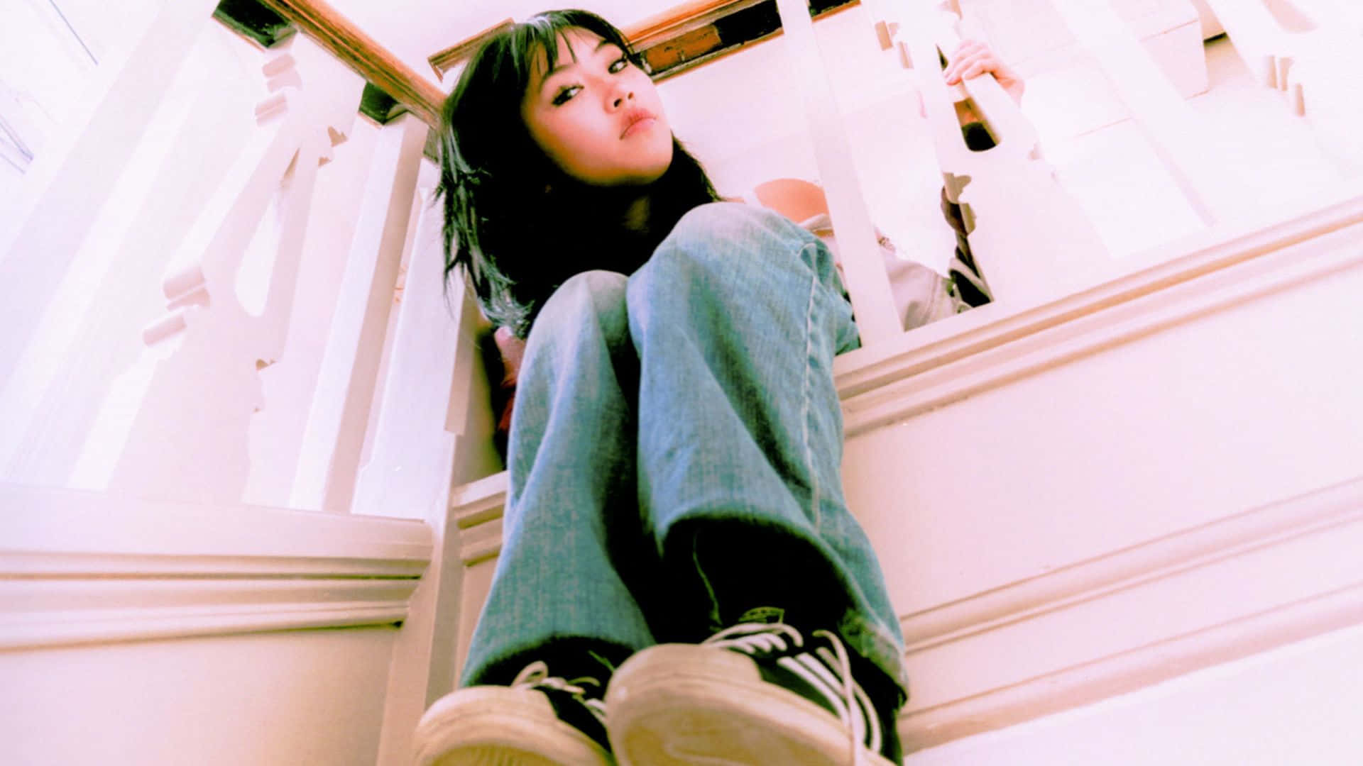  壁紙 — 一位黑髮年輕女性隨意地坐在白色樓梯上，冷靜地向下看著相機。