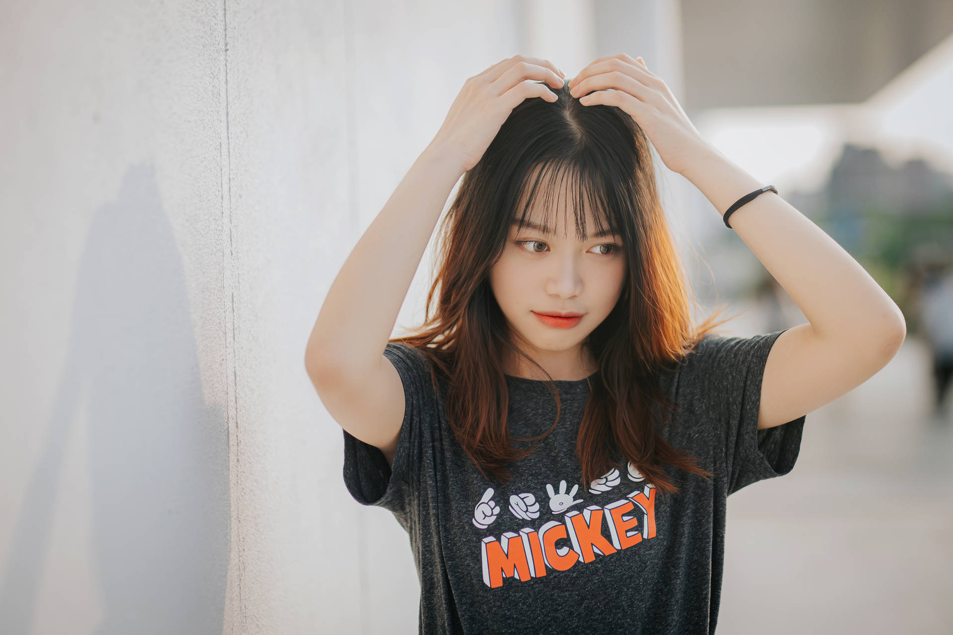 穿著米奇老鼠T恤的年輕女性在白色牆壁附近觸碰頭髮。