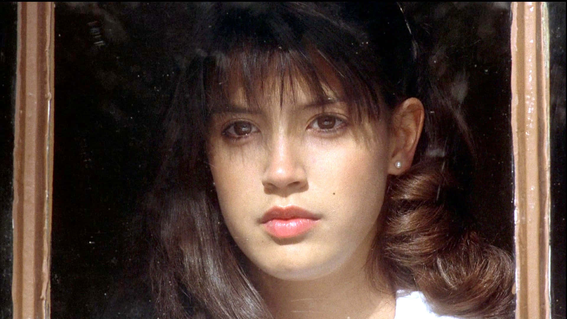 Phoebe Cates 桌布 壁紙 — 一位黑髮戴珍珠耳環的年輕女子，透過風化的木窗框凝視著。