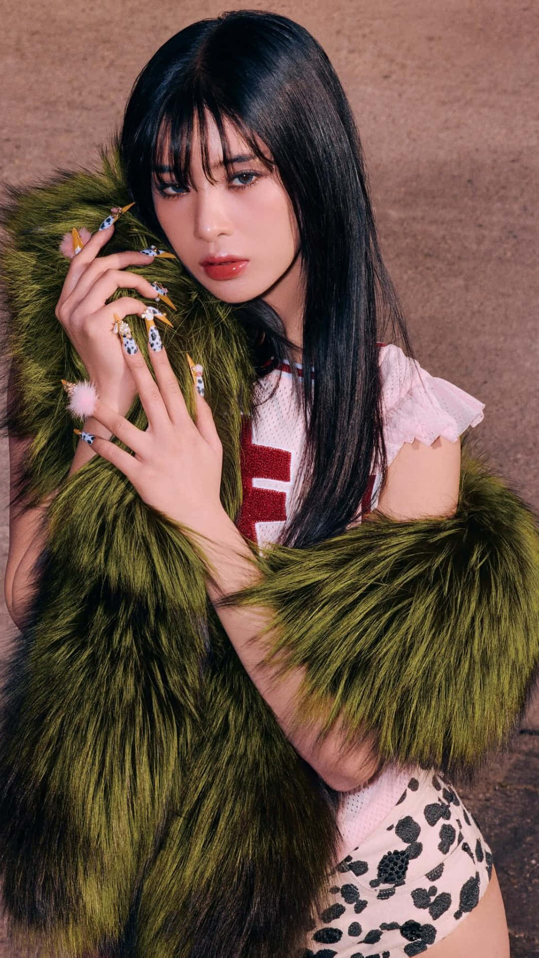  壁紙 — 一位年輕女性留著黑色長髮，穿著寬鬆的綠色毛皮大衣和圖案服裝，擺出華麗的美甲姿勢。