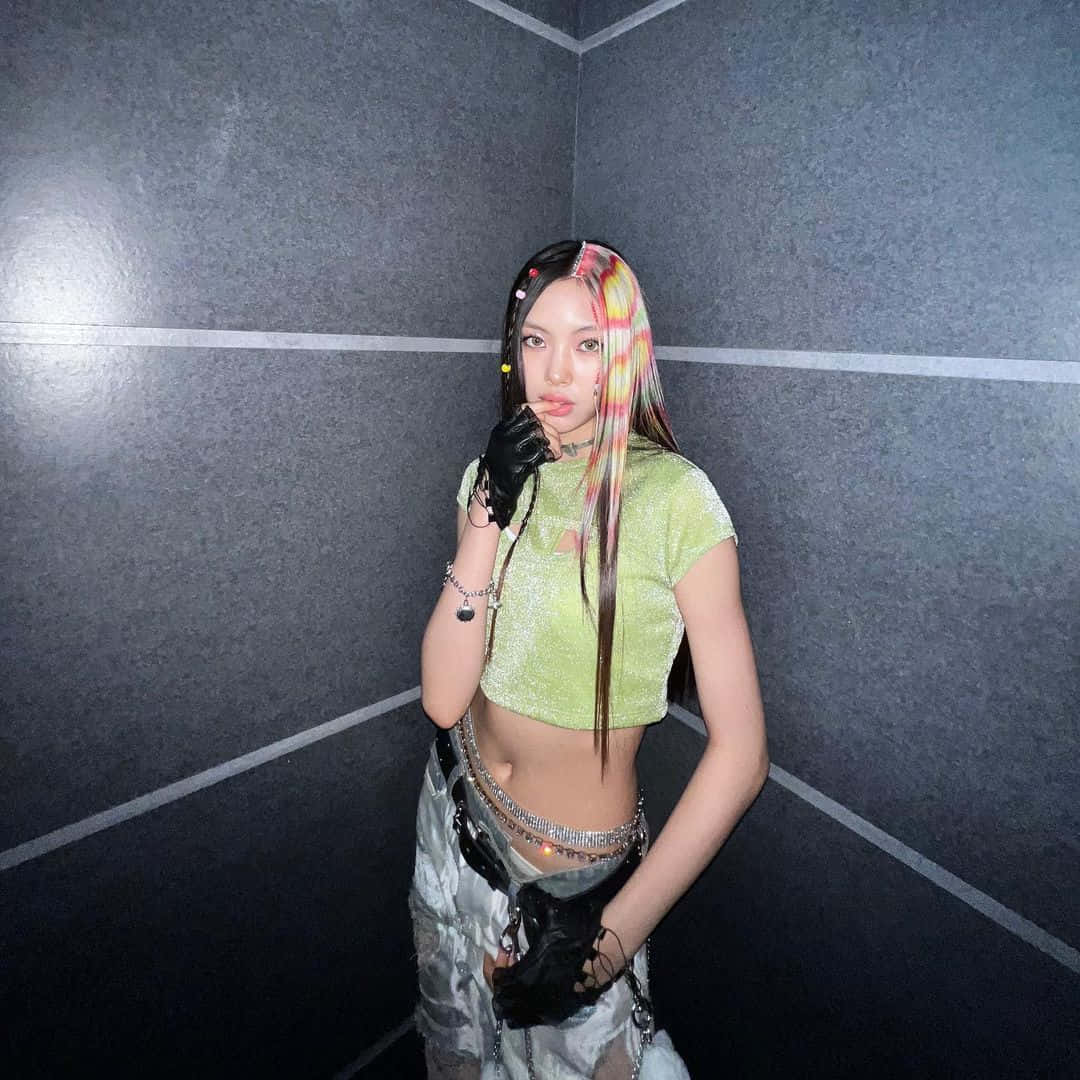  壁紙 — 一位年輕女性，擁有充滿活力的彩虹色頭髮和黑色手套，在光線昏暗的灰色瓷磚角落自信地擺姿勢。