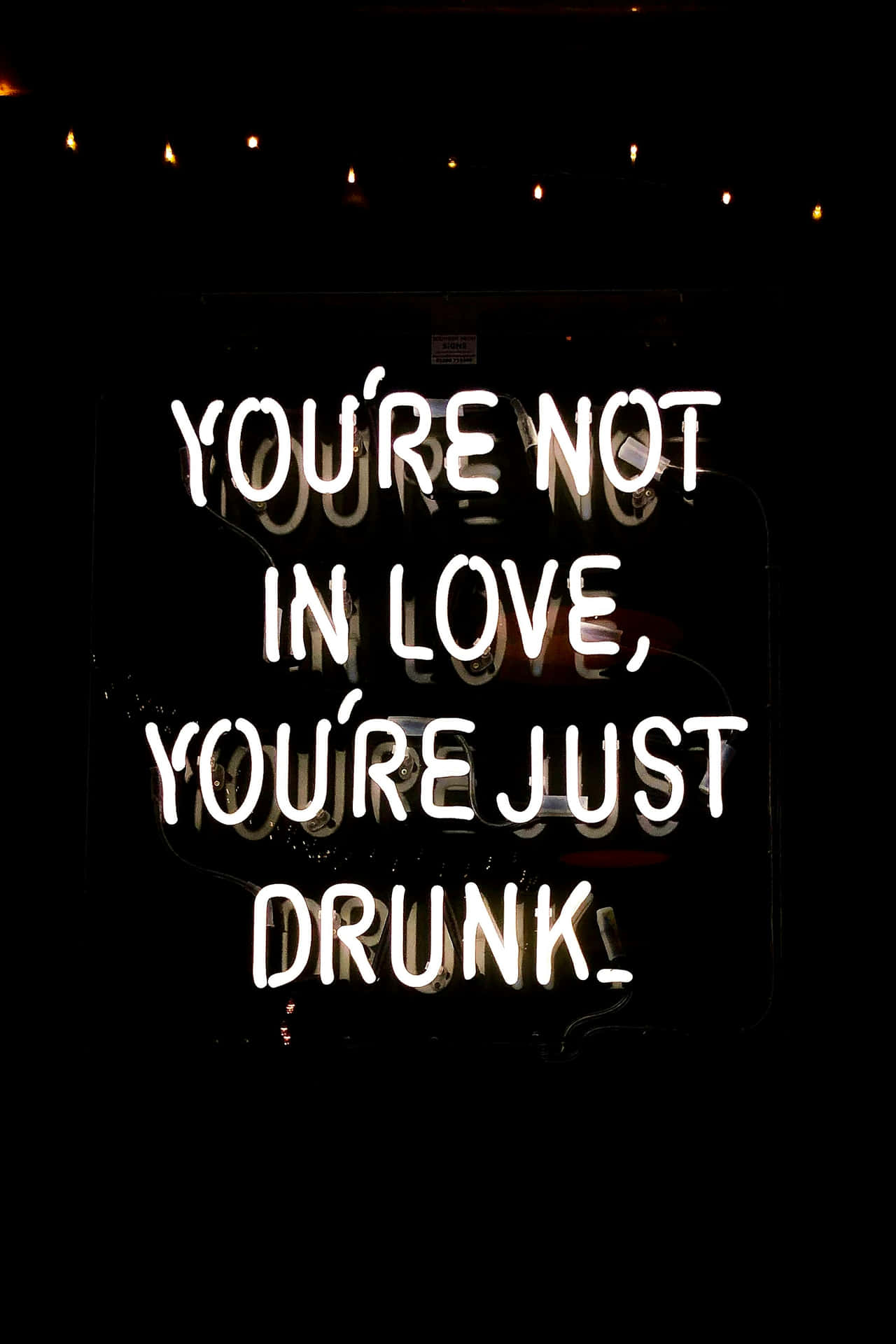  壁紙 — 一個發光的白色霓虹燈牌寫著「YOU'RE NOT IN LOVE, YOU'RE JUST DRUNK」，背景為深色，上方有串燈。