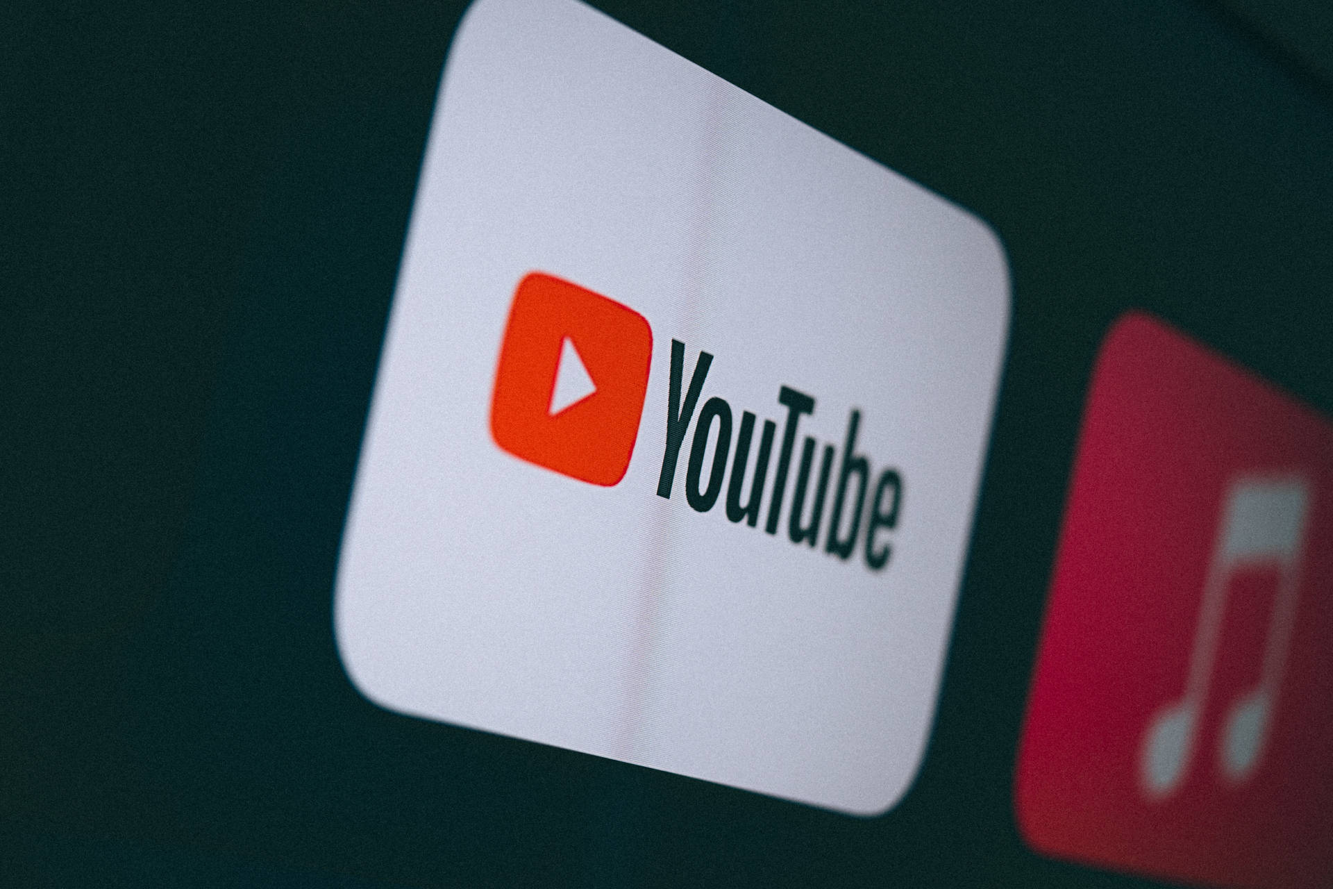 YouTube 應用程式圖示在黑暗的數位螢幕上發光，附近有一個模糊的音樂應用程式圖示。