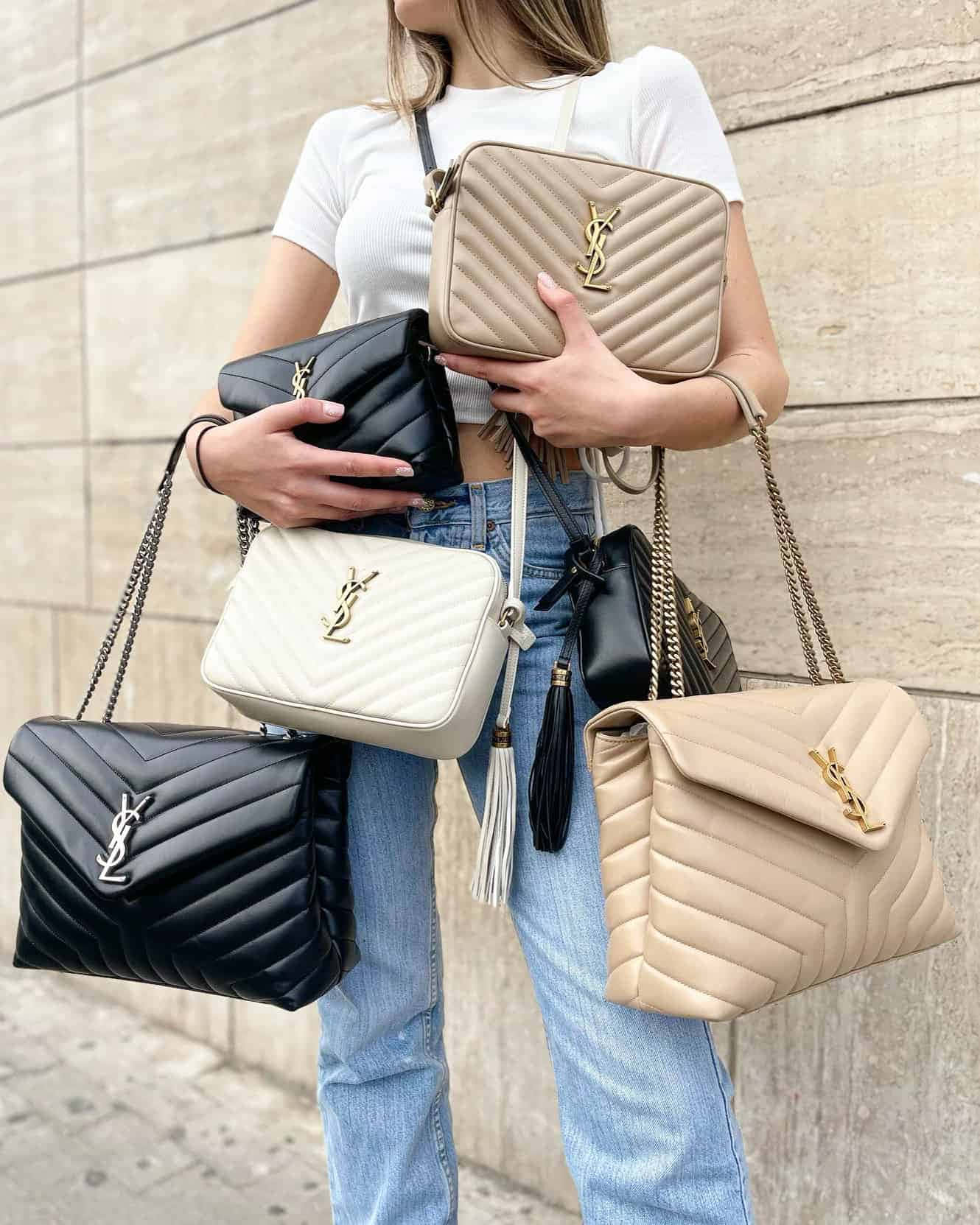 YSL，時尚與優雅的完美結合 壁紙 — 一位身穿白色T恤和牛仔褲的女性，在石牆前手持多個黑色、白色和米色的絎縫YSL手袋。