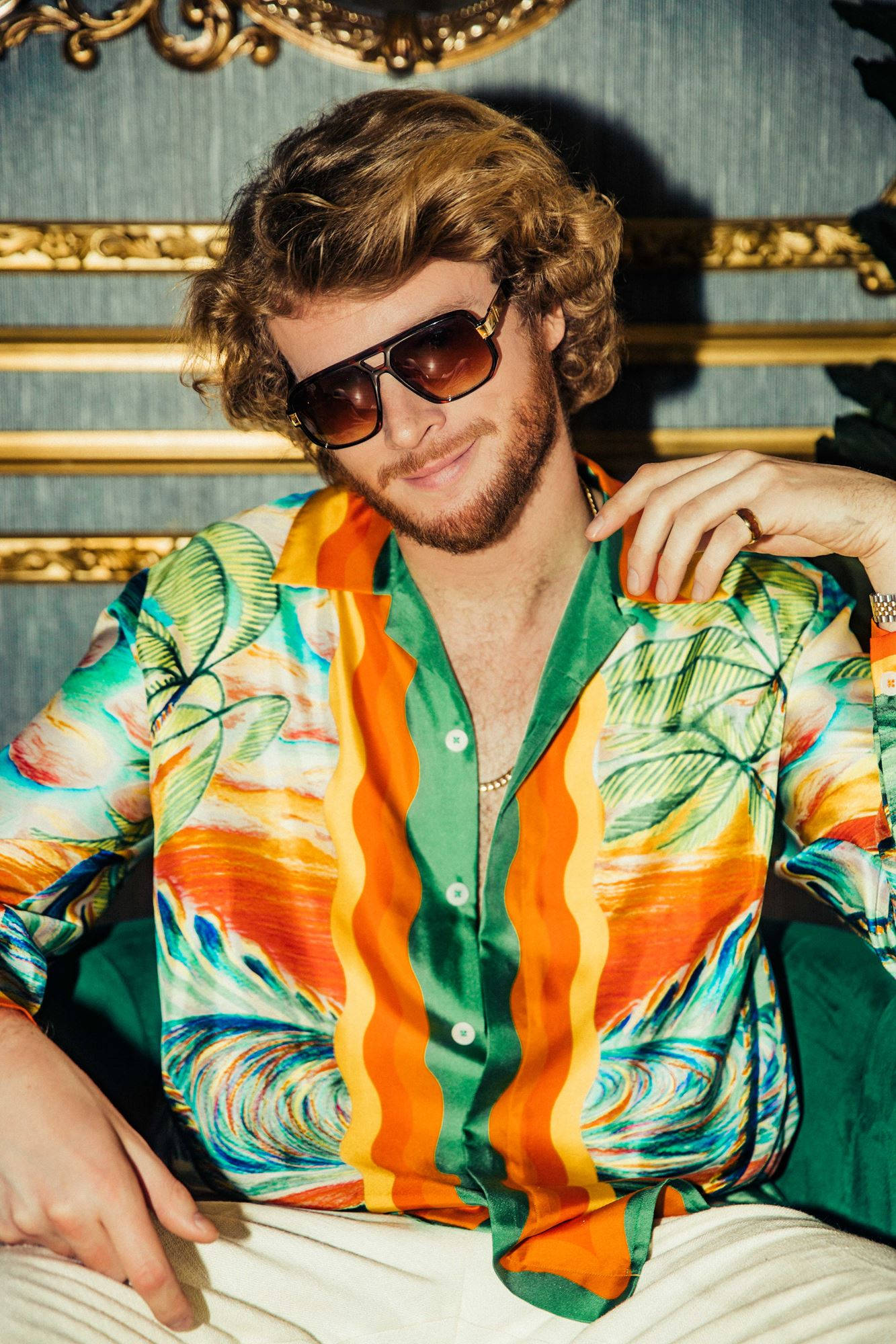 Yung Gravy 廣告宣傳照封面 壁紙 — 一位時尚男士，捲髮戴太陽眼鏡，身穿鮮豔熱帶襯衫，背景是金色邊框的藍色牆紙。