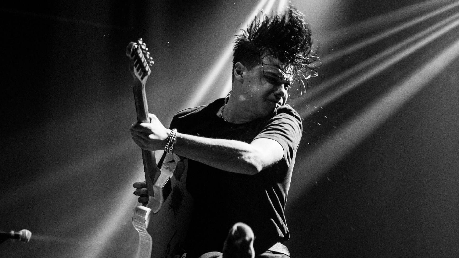 Yungblud 吉他獨奏 壁紙 — 一張黑白照片，捕捉一位結他手在表演中，帶有刺蝟頭和舞台燈光劃破空氣的瞬間。