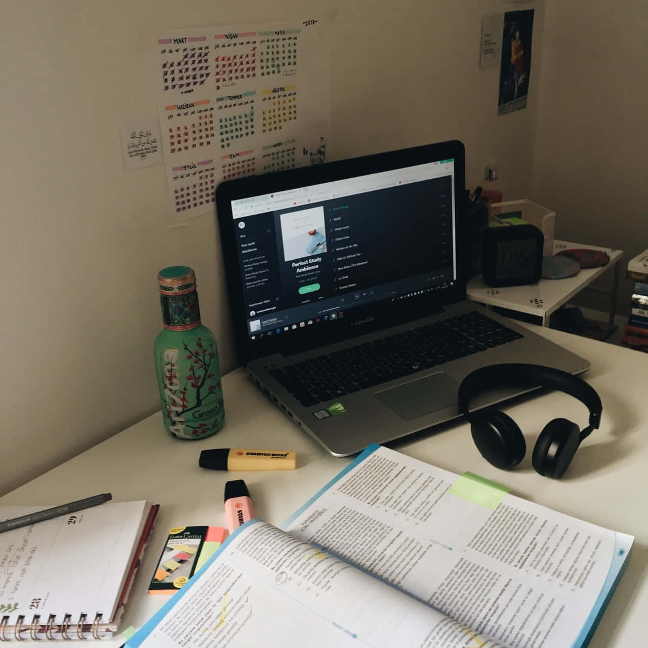  壁紙 — 一張雜亂的書枱，上面放著一本打開的教科書、螢光筆、耳機和一部顯示學習應用程式的筆記型電腦。