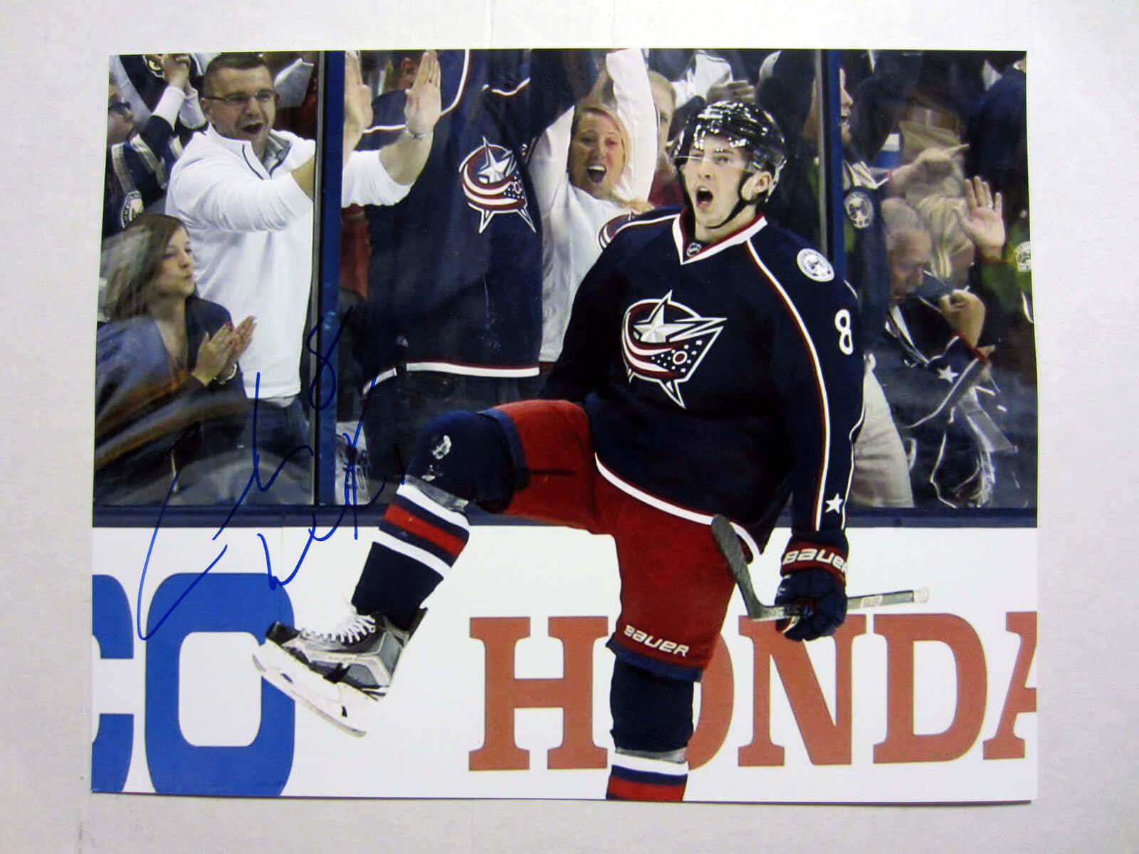 Zachary Werenski 勝利瞬間 壁紙 — 一名身穿哥倫布藍夾克球衣的冰球運動員在玻璃後球迷歡呼聲中舉起腿慶祝。