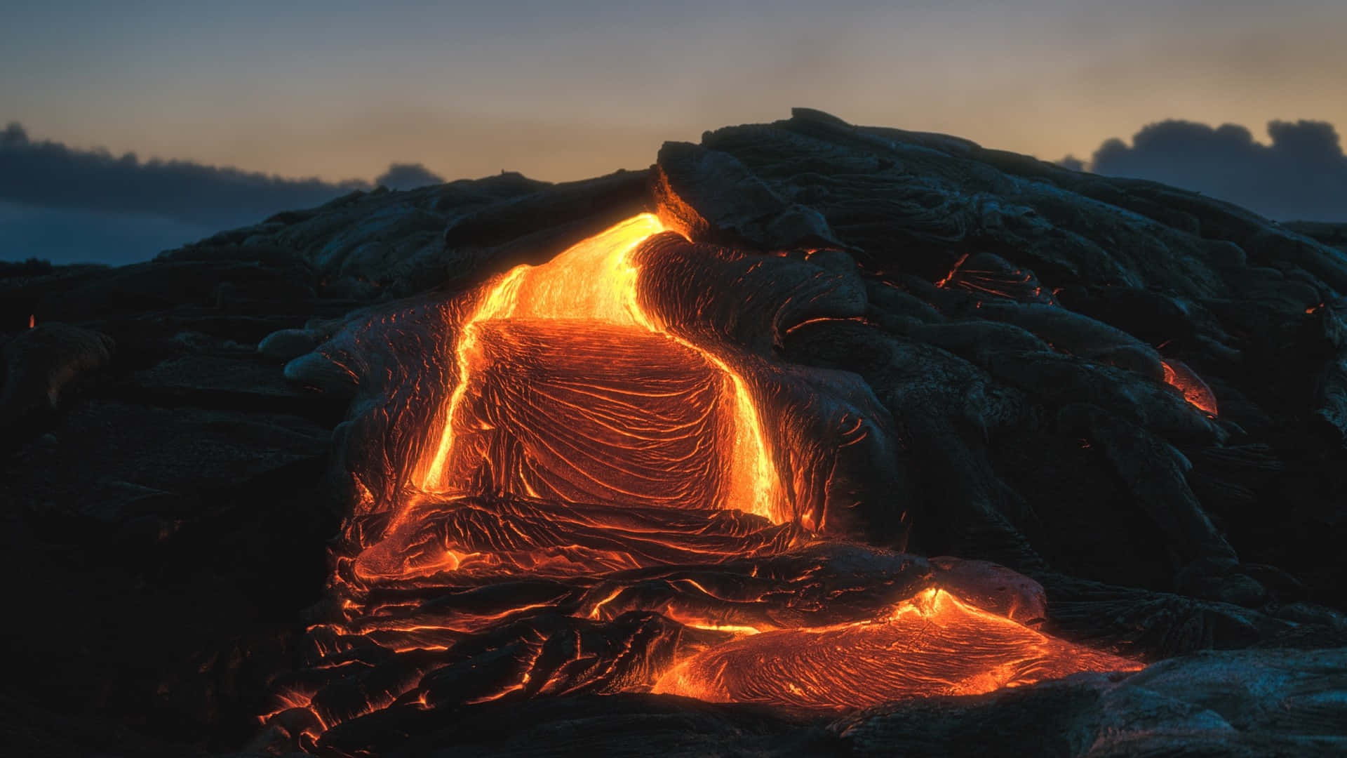 熔岩流在暮色中沿著黑暗的火山地形發出橙色光芒。