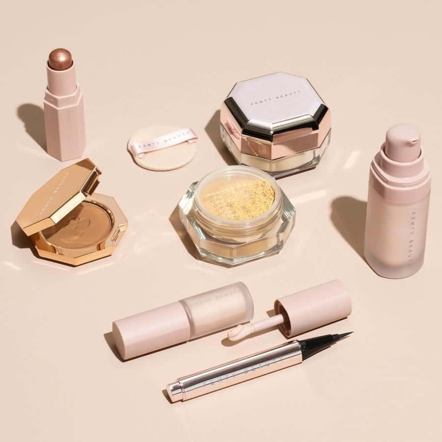 在米色背景上，以玫瑰金和裸色調的Fenty Beauty化妝品系列。