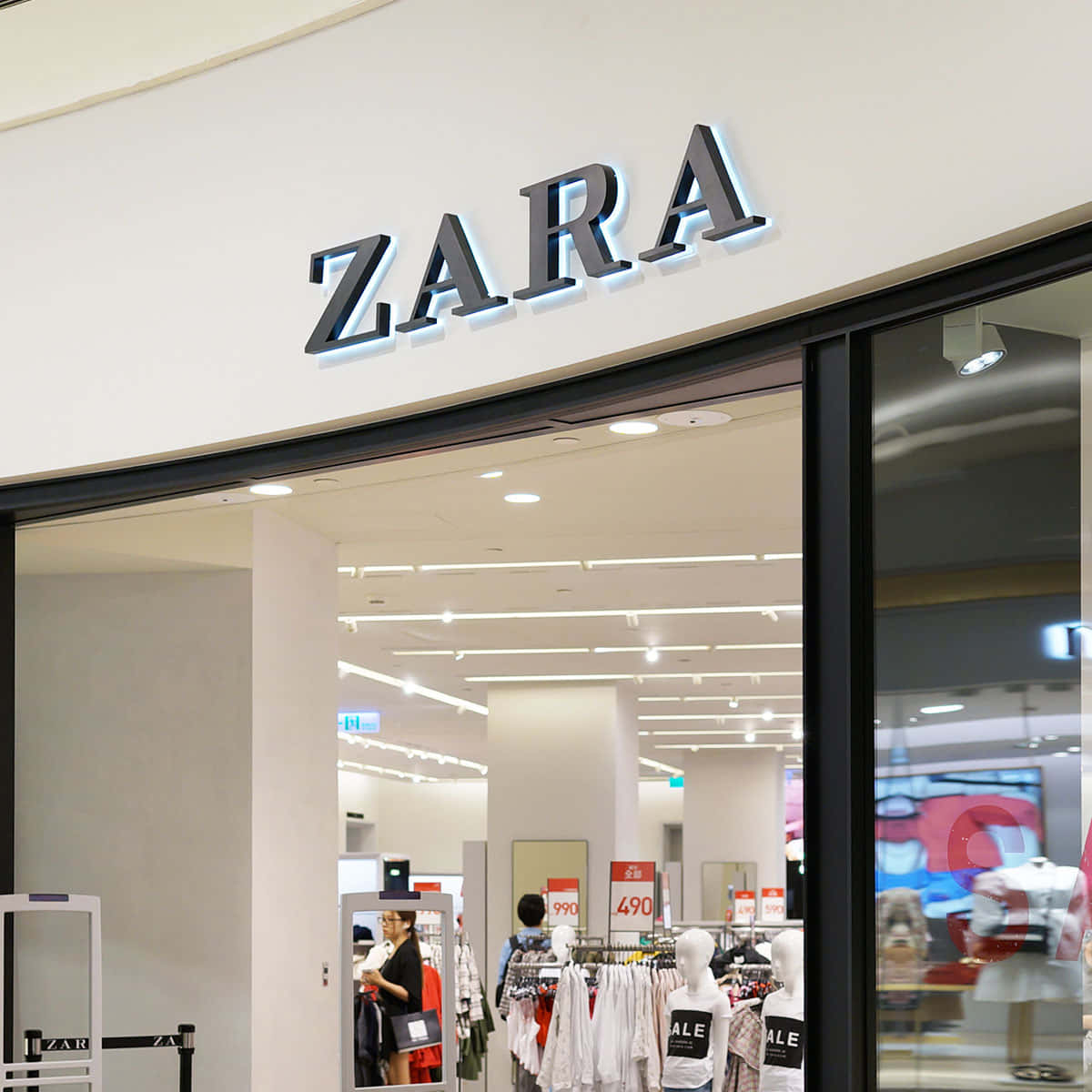 以Zara最新潮流時尚展現個人風格 壁紙 — 現代Zara商店入口，配備玻璃門和明亮內部，展示服裝架和模特兒。