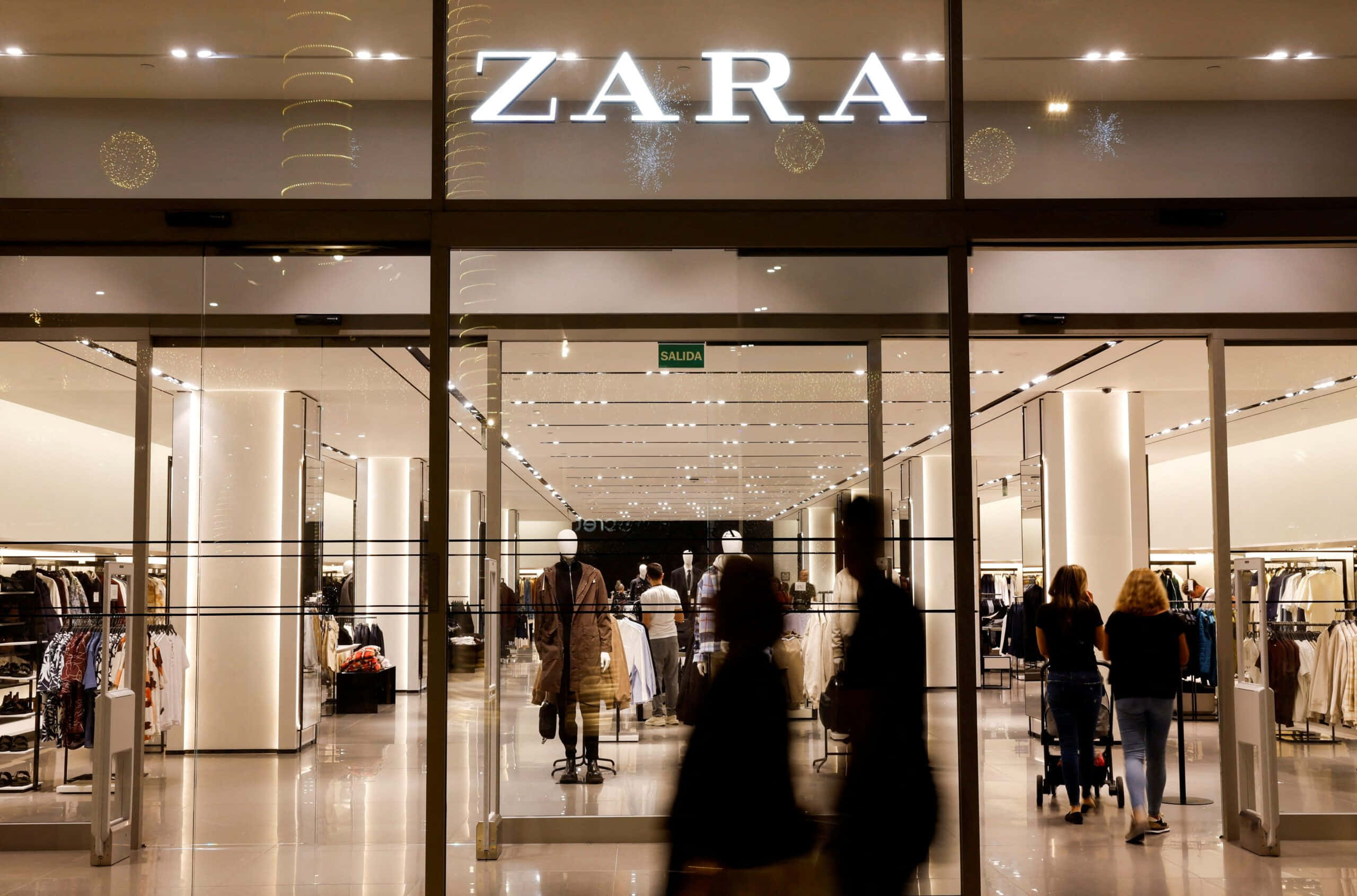 「永不過時的風格 — ZARA 最新系列」 壁紙 — Zara 店舖入口，設有玻璃門及明亮室內燈光，顧客進進出出。