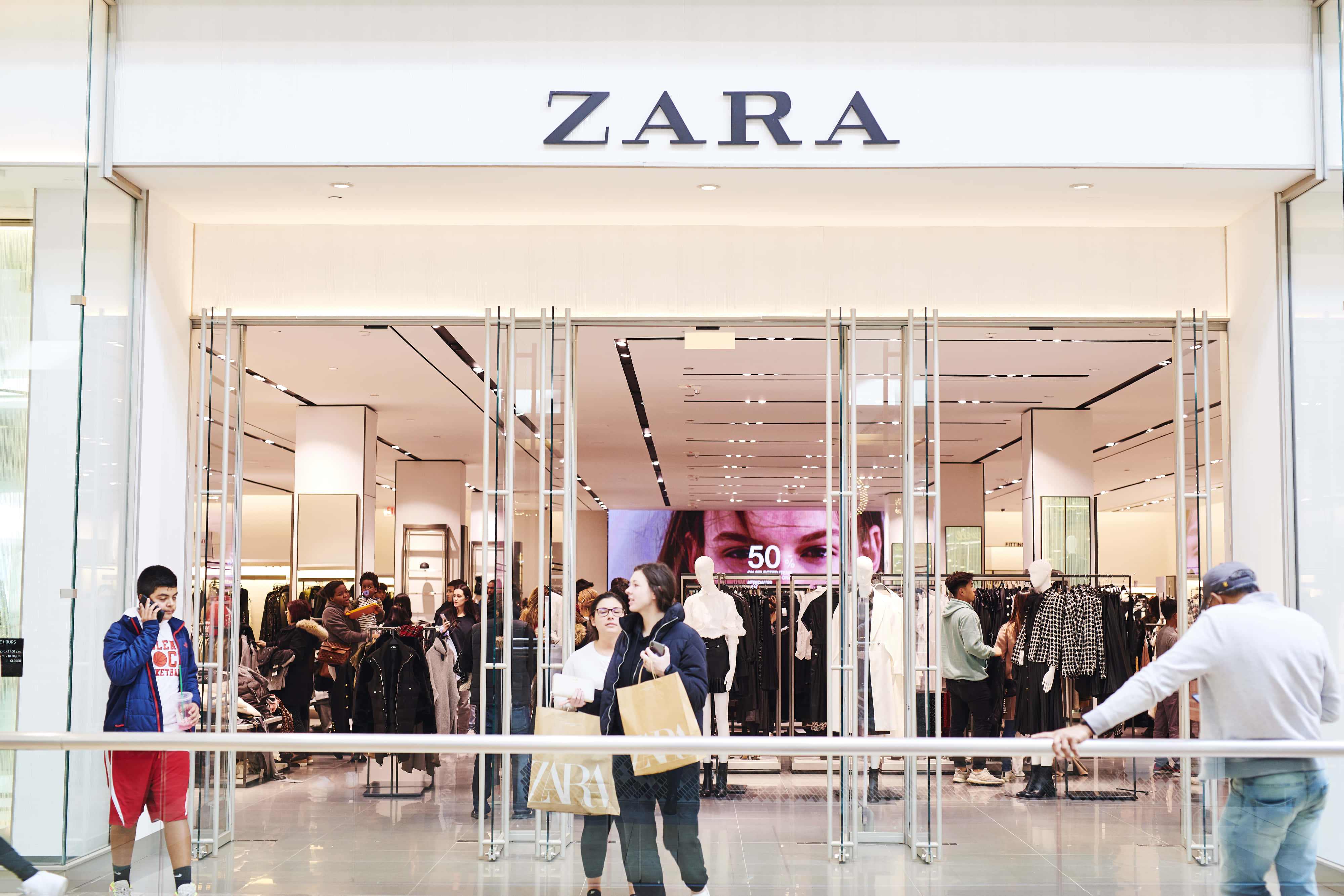 時尚與潮流：Zara 的最新趨勢 壁紙 — 購物者瀏覽並進入一間明亮現代的Zara商店，店內有玻璃門和可見的衣架。