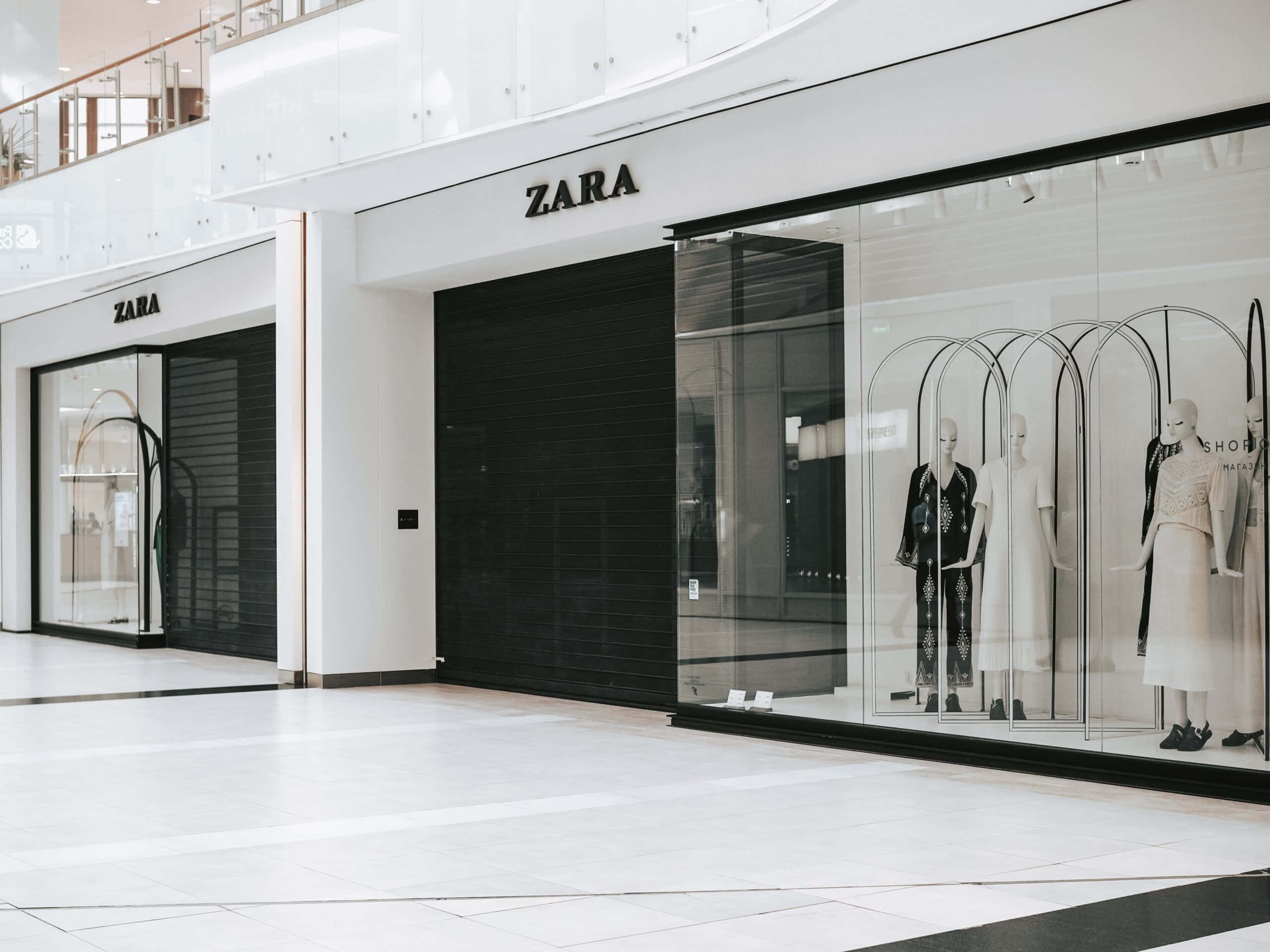 Zara時尚服飾，適合任何場合 壁紙 — 一間時尚的Zara商店，配有黑色百葉窗和玻璃窗，在明亮的現代購物中心內展示穿著簡約黑白服裝的人體模型。