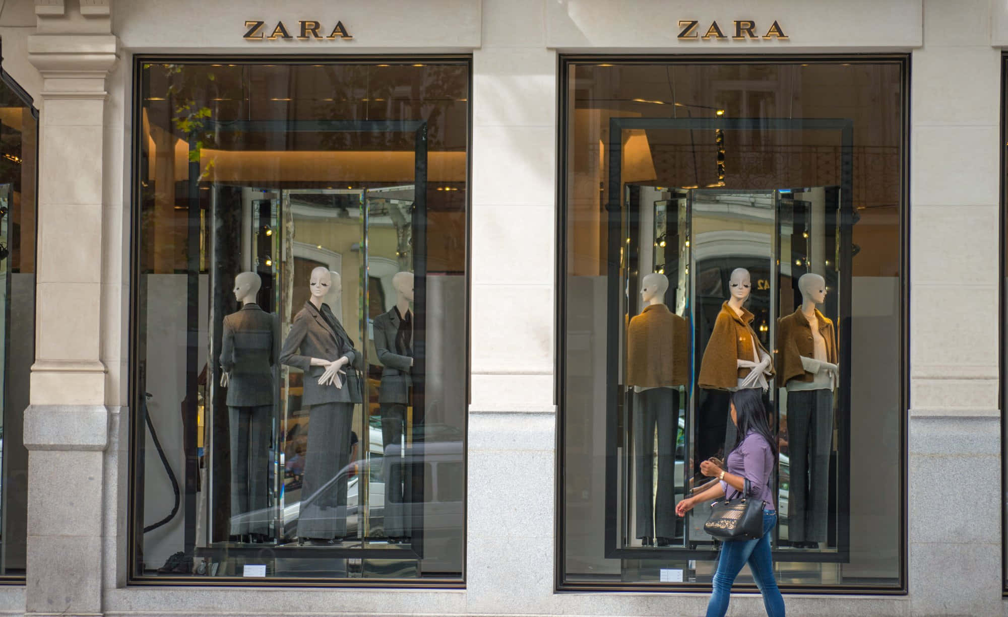 Zara最新時尚趨勢 壁紙 — 一位女士走過兩個Zara商店櫥窗，櫥窗內展示穿著訂製西裝和外套的人體模型。