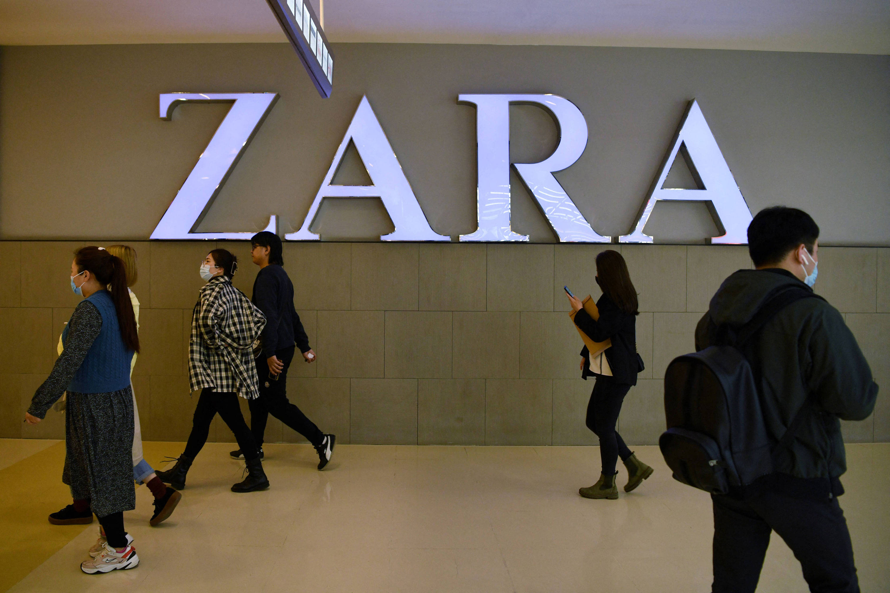 ZARAOutlet招牌 壁紙 — 戴著口罩的人們走過現代購物中心內部一個大型發光的ZARA商店標誌。
