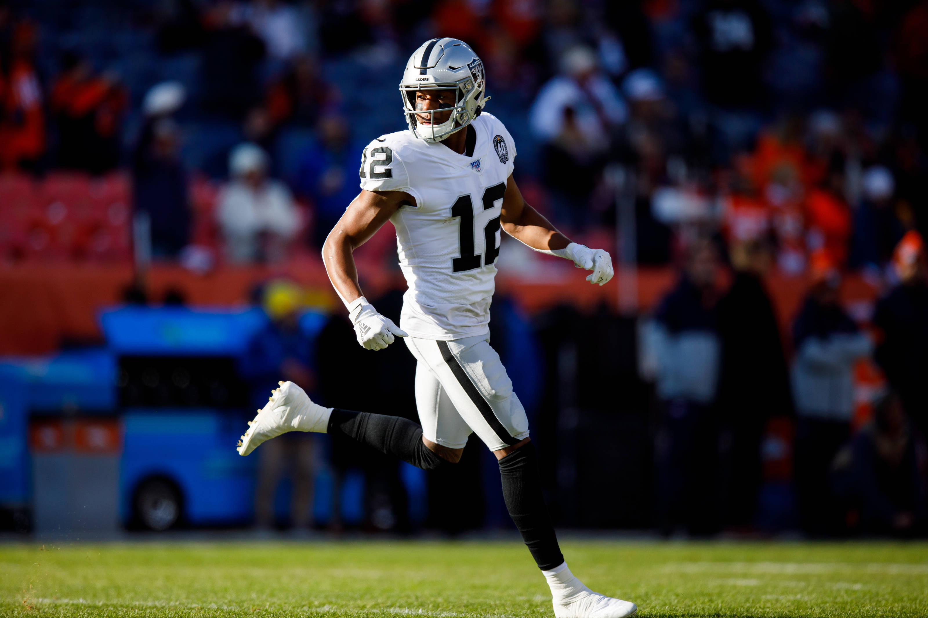 Zay Jones 在足球場奔跑 壁紙 — 一名身穿白色12號球衣的足球運動員在陽光明媚的綠色球場上衝刺，背景是模糊的體育場觀眾。