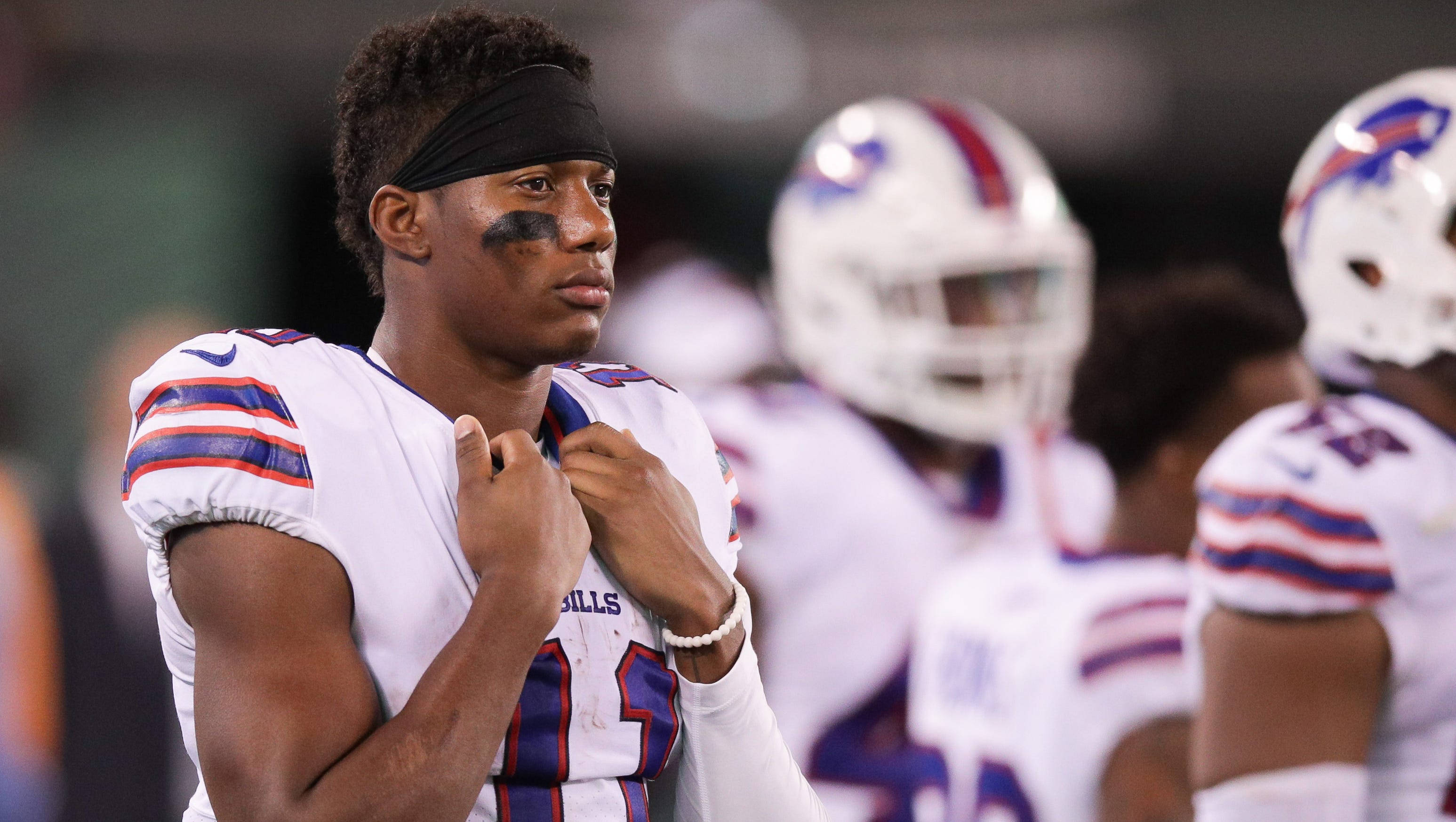 Zay Jones 水牛隊白球衣 壁紙 — 一位專注的Buffalo Bills美式足球員在球場燈光下調整球衣，背景有隊友模糊的身影。