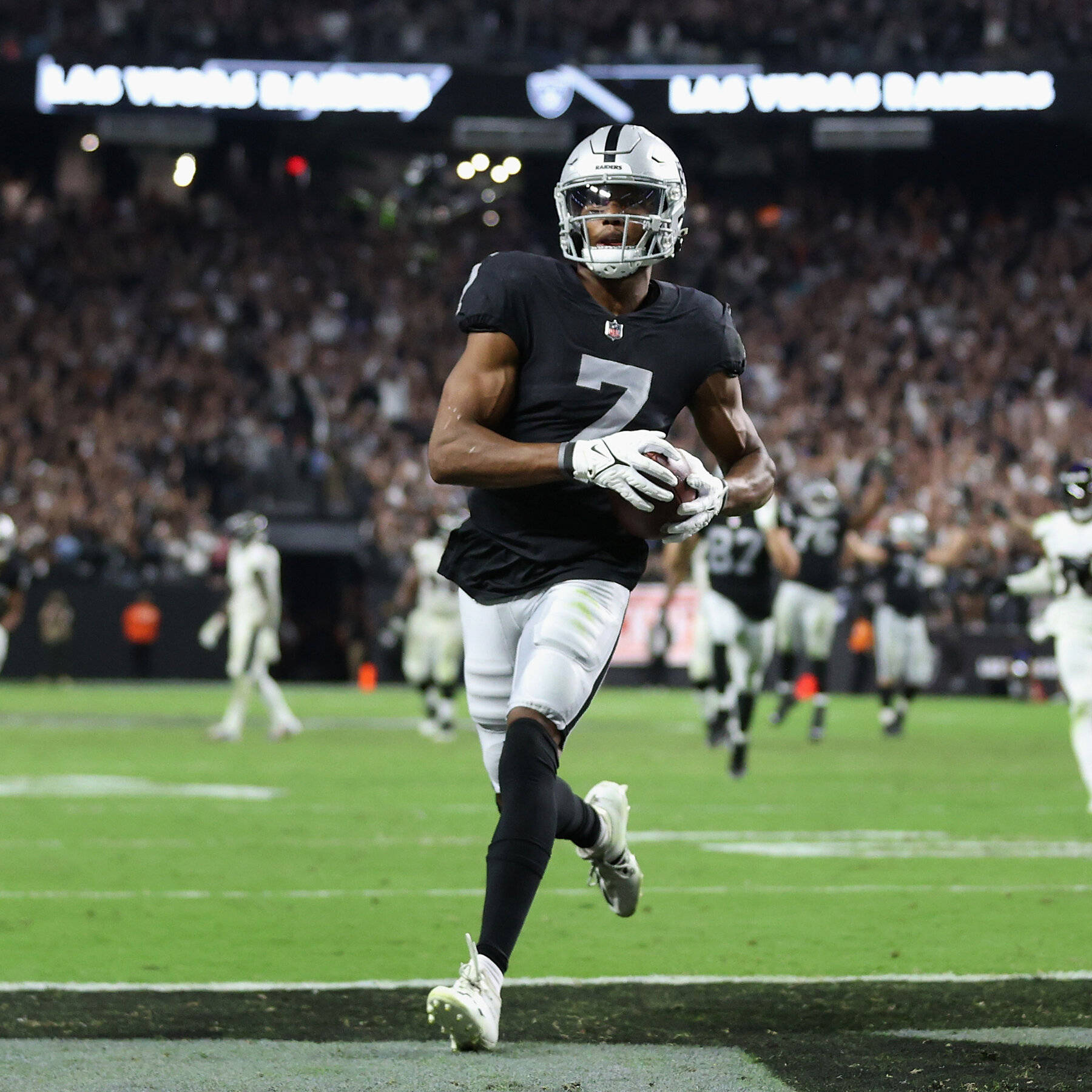 Zay Jones 黑色突襲者球衣 壁紙 — 一名身穿黑銀色球衣的拉斯維加斯突襲者美式足球員，在明亮的燈光下，帶著球衝過擠滿觀眾的體育場。