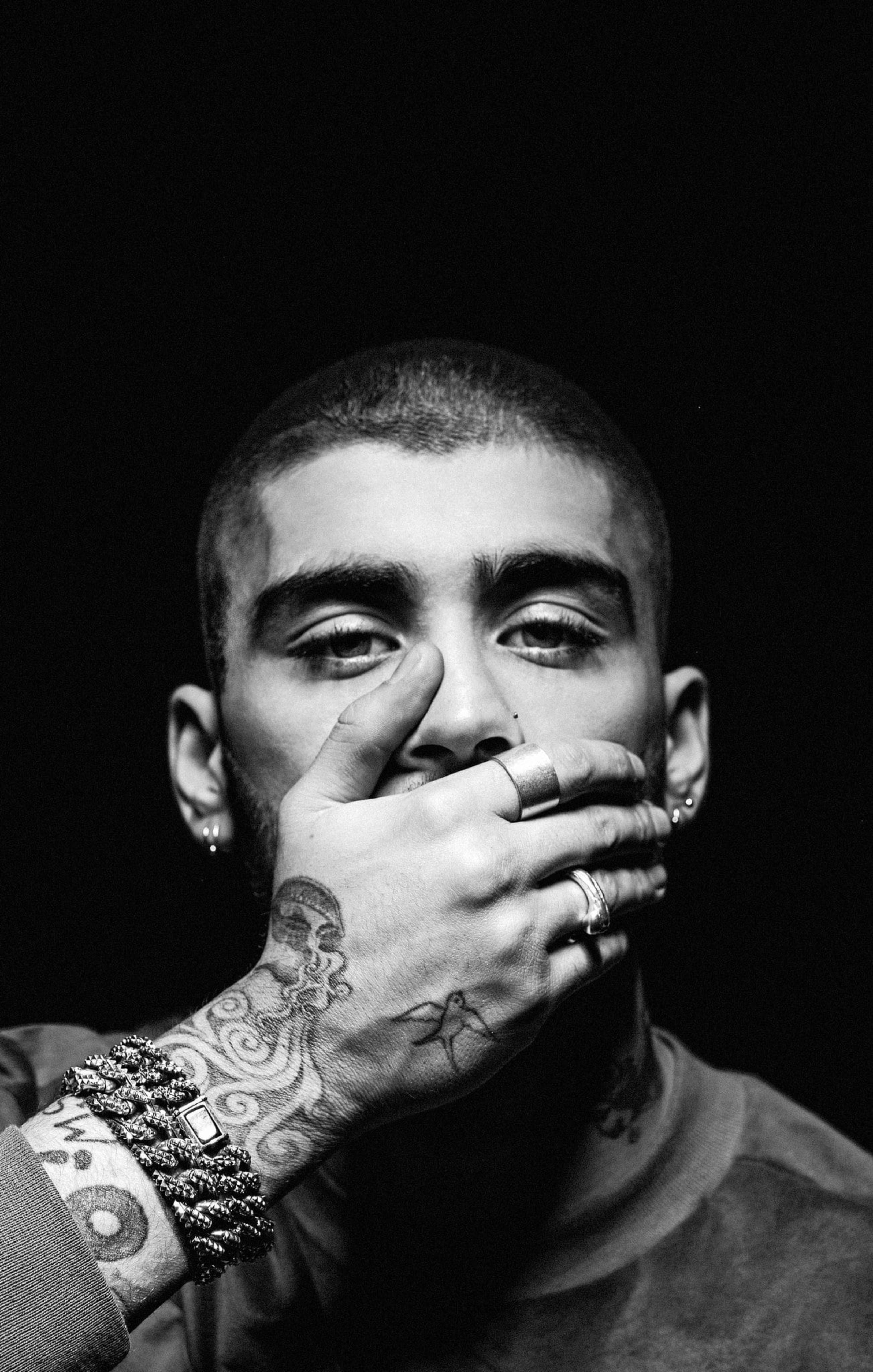Zayn Malik《紐約時報》2016年專訪 壁紙 — 一個黑白肖像，一個男人手上和手腕上有紋身，用手遮住嘴巴，背景黑暗。