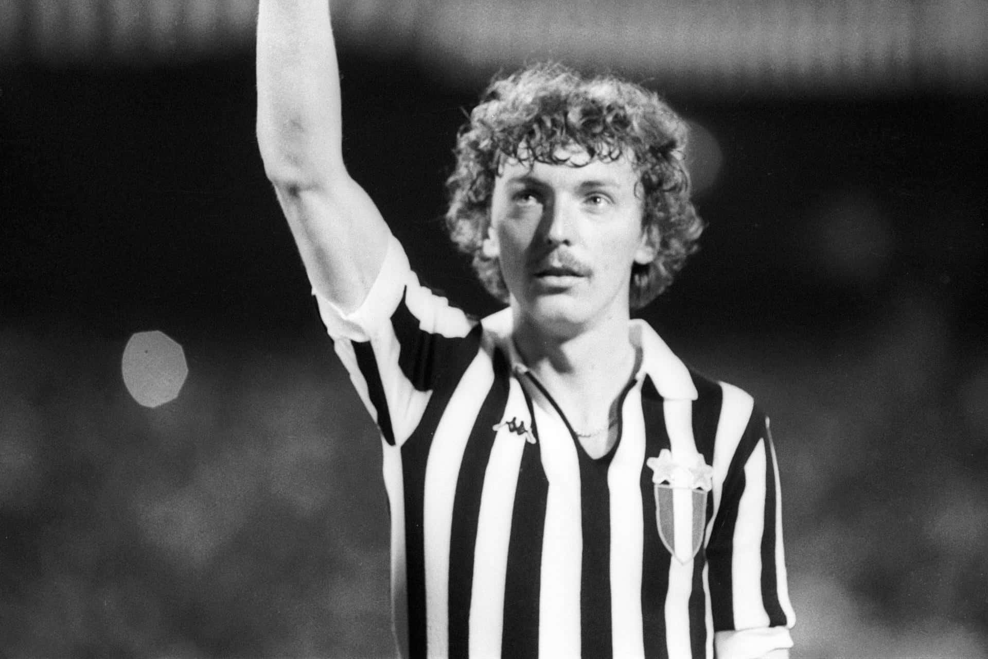 Zbigniew Boniek 身穿尤文圖斯黑白豎條球衣 壁紙 — 一張黑白照片，拍攝一名穿著條紋球衣的捲髮足球員在體育場內舉起手臂。