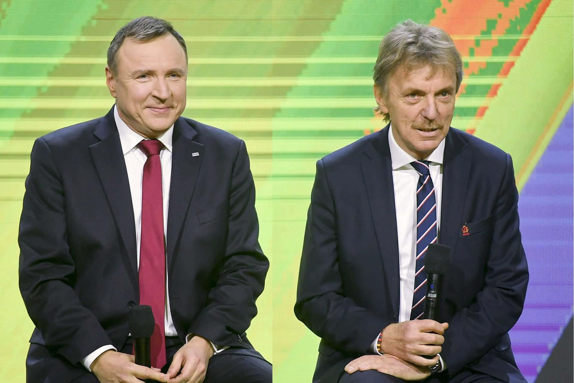 Zbigniew Boniek 與 Jacek Kurski 同框 壁紙 — 兩名身穿西裝的男子並排坐在舞台上，手持麥克風，背景是充滿活力的綠色和橙色數位背景。