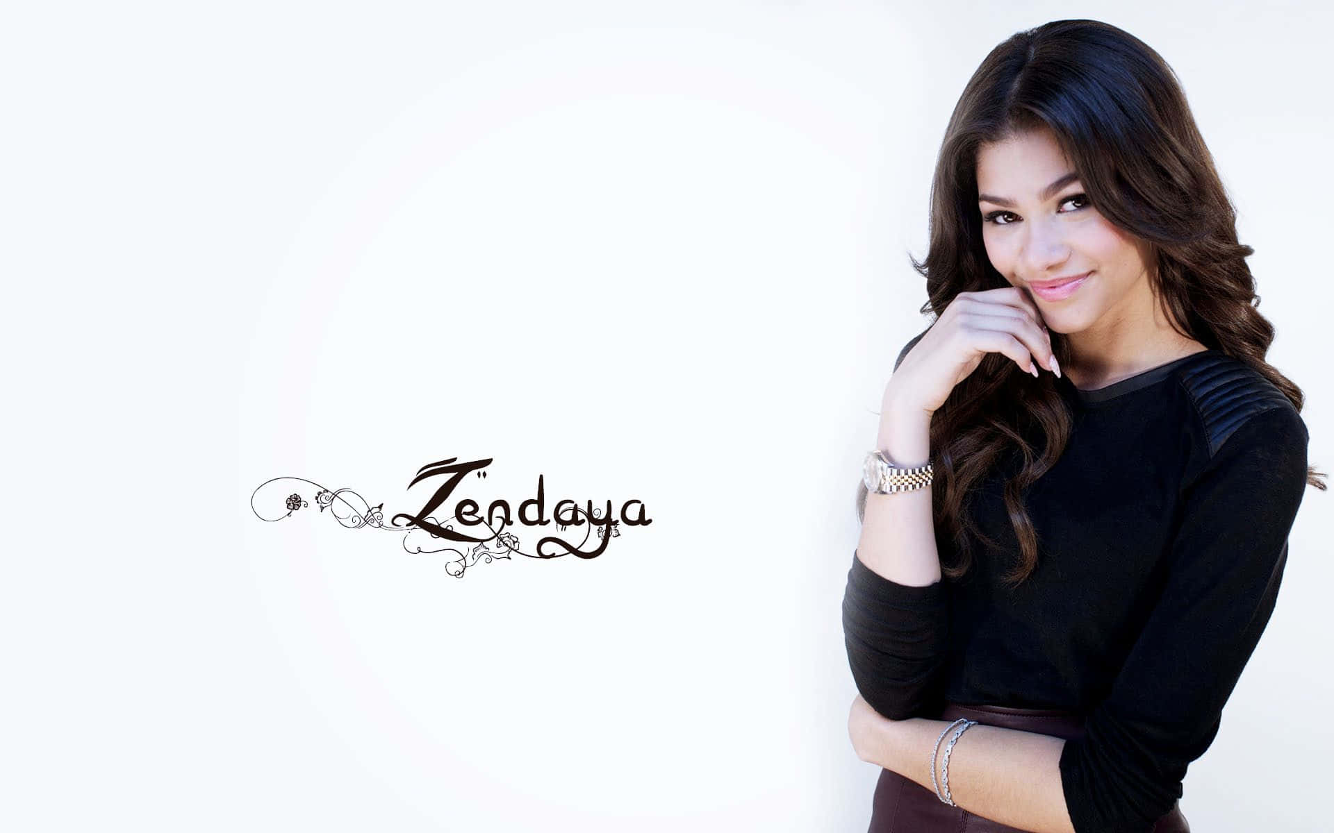 Zendaya 歌手高清壁紙 壁紙 — Zendaya 喺乾淨嘅白色背景前擺出溫柔嘅笑容，佢嘅深色捲髮框住佢嘅臉，下巴擱喺手上。