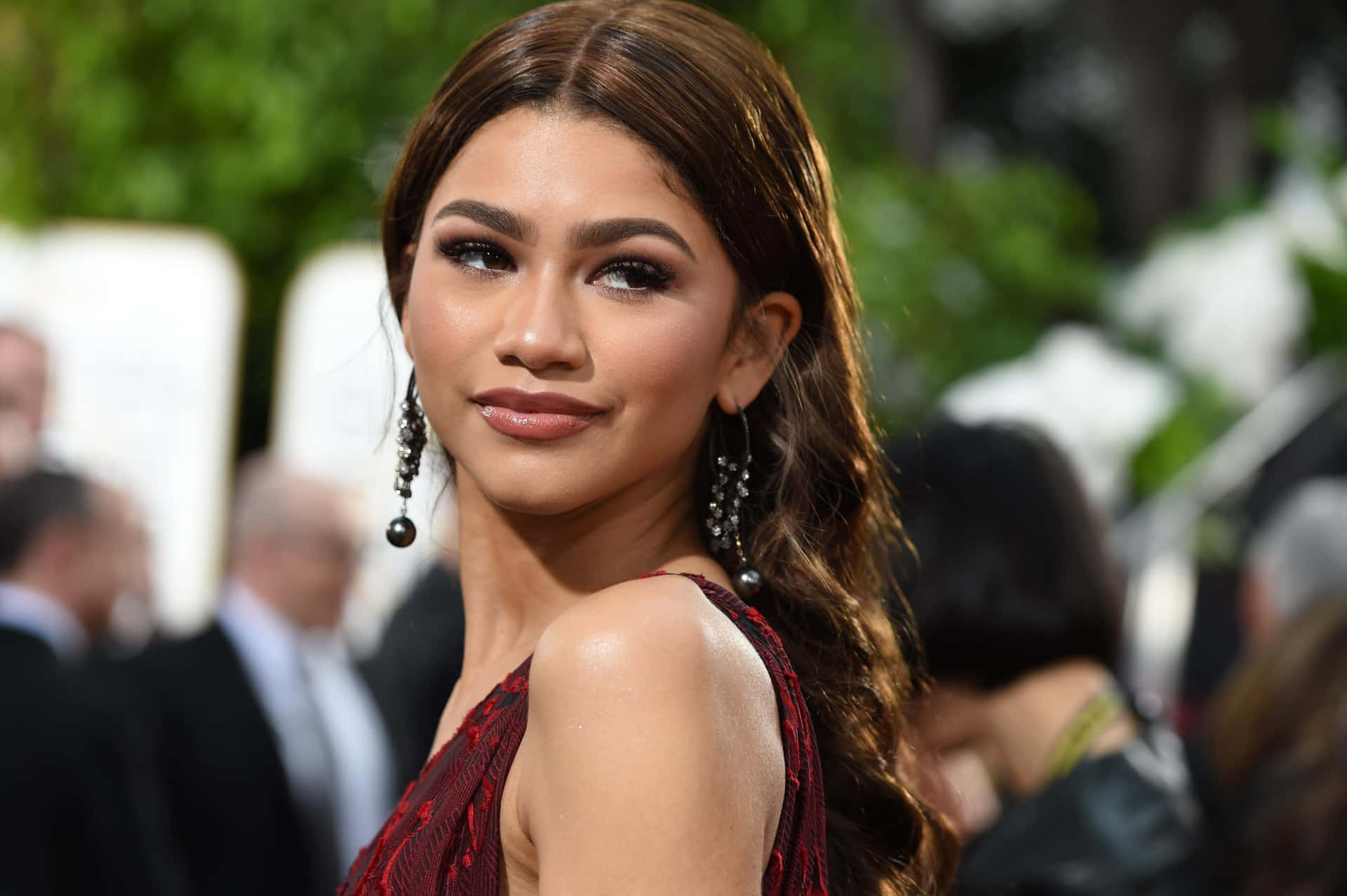 Zendaya 身穿紅色連衣裙在戶外活動中對著鏡頭微笑。