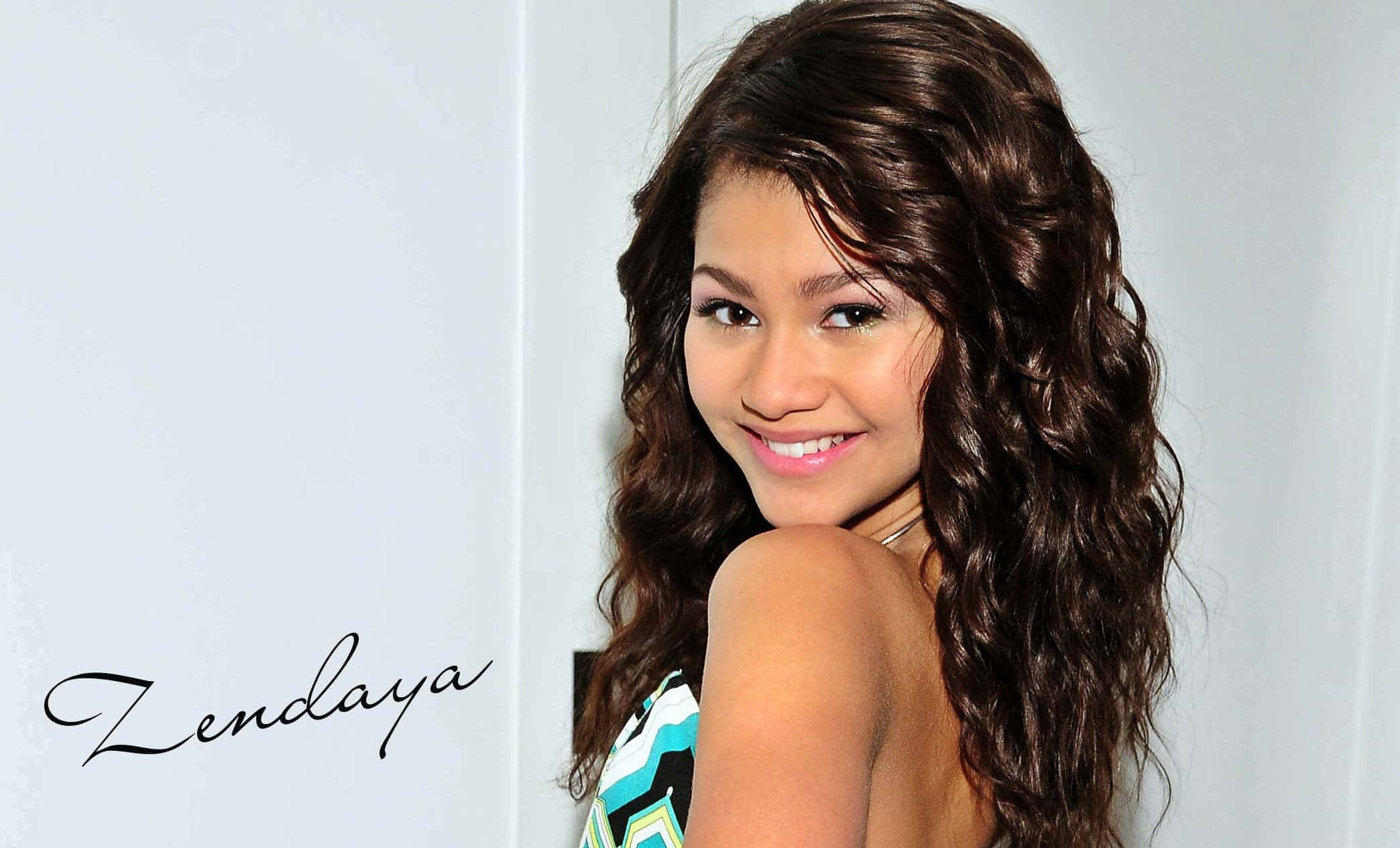 Zendaya 桌布 壁紙 — Zendaya 喺純白色背景前，留住長長嘅波浪形棕色頭髮，露出溫暖嘅笑容。