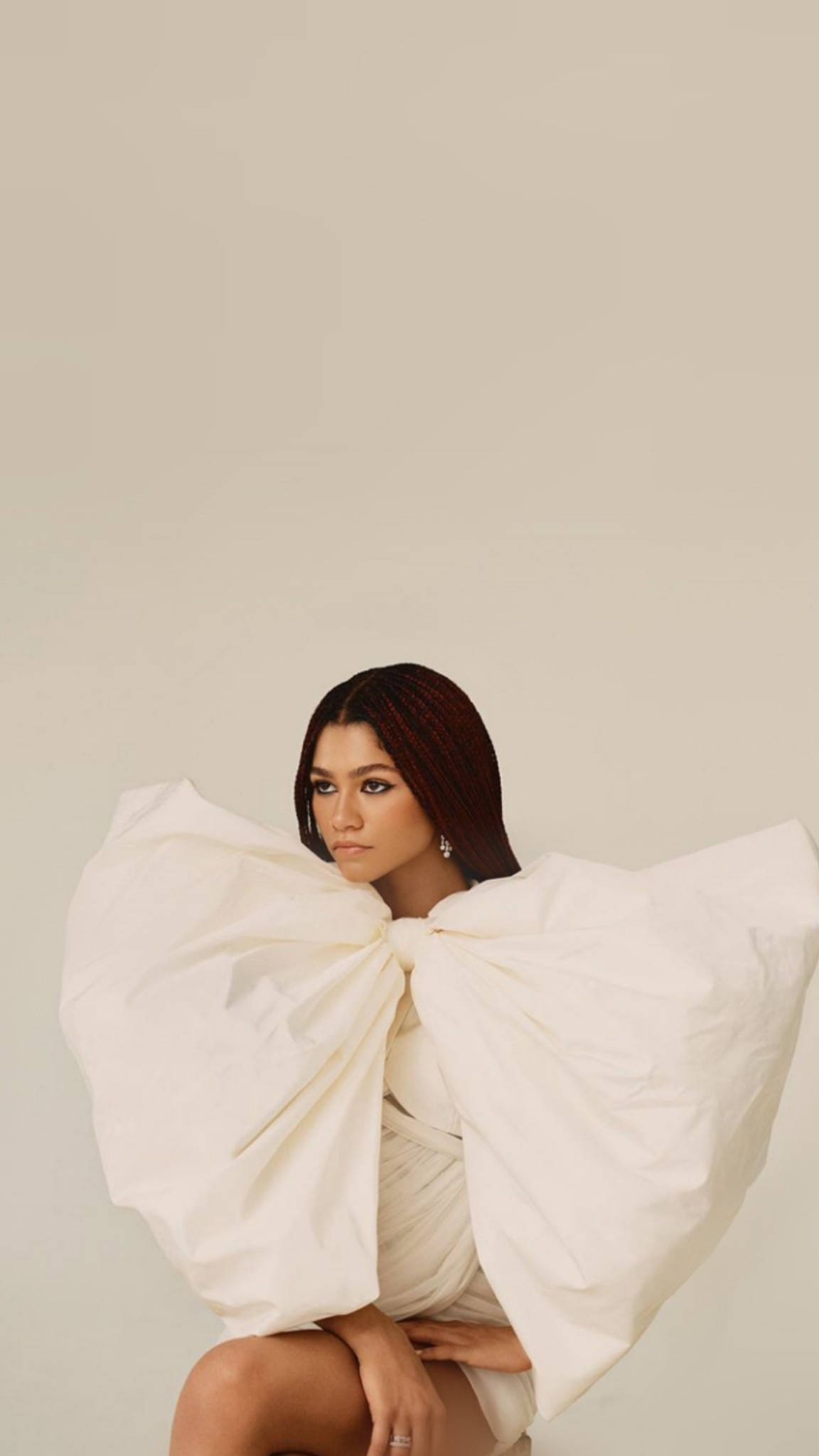 Zendaya 為《Elle USA》拍攝封面 壁紙 — 一位辮子頭髮的女性，穿著白色大蝴蝶結連衣裙，平靜地坐在純米色背景前。