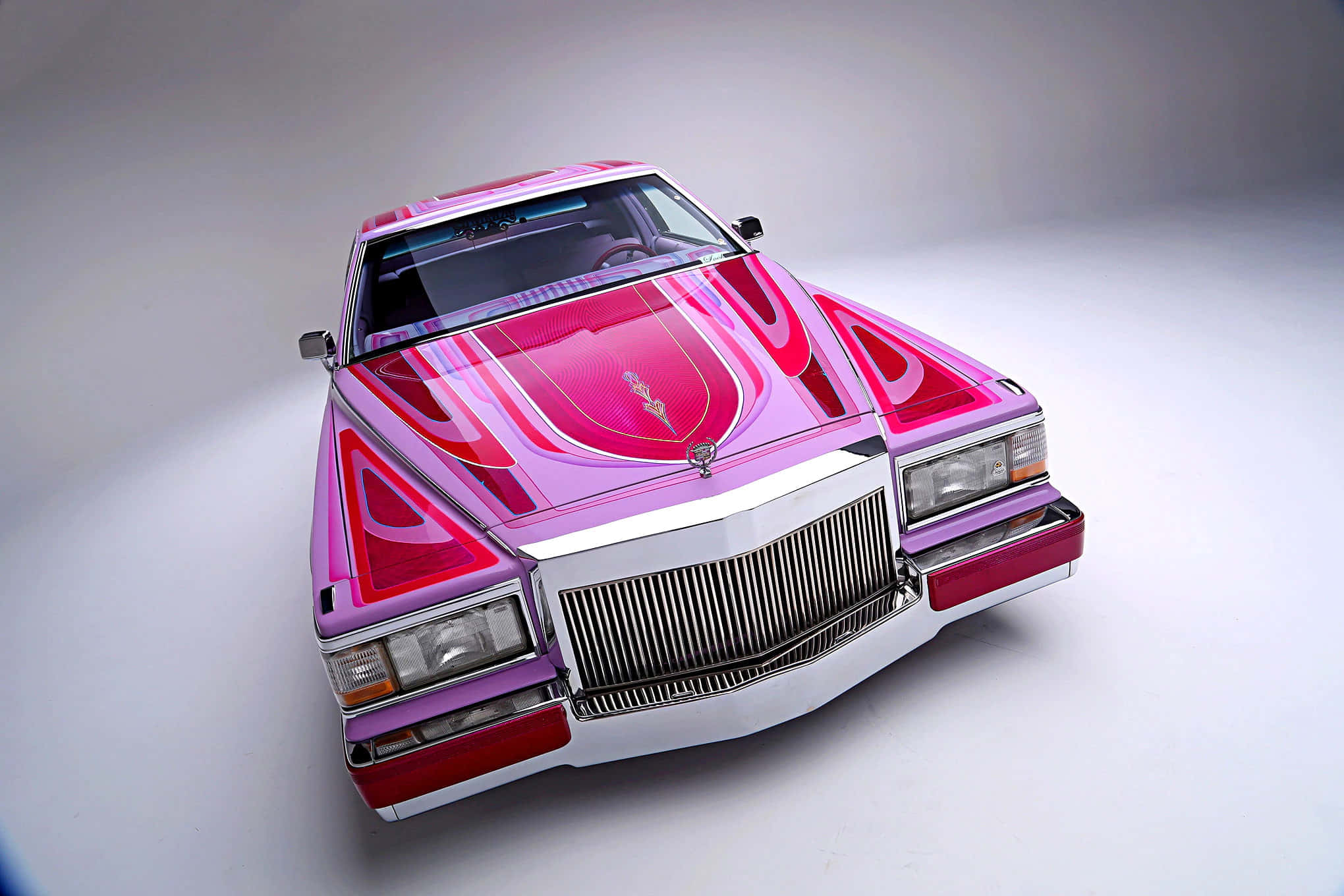Cadillac Fleetwood 桌布 壁紙 — 一張高角度攝影棚拍攝的經典凱迪拉克，帶有光澤的粉紅色和紅色火焰貼花，背景為白色。
